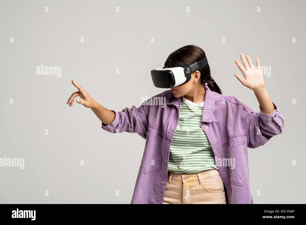 Eine Frau mit virtueller Brille spielt Videospiel-Punkte Zeigefinger auf Kopierbereich auf grauem Hintergrund. Stockfoto