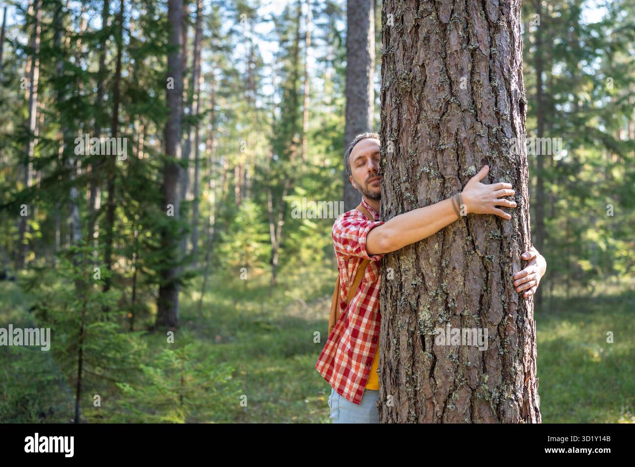 Entspannter Mann umarmt den Baumstamm in die Natur im Wald mit geschlossenen Augen, die die Umwelt schützen. Stockfoto