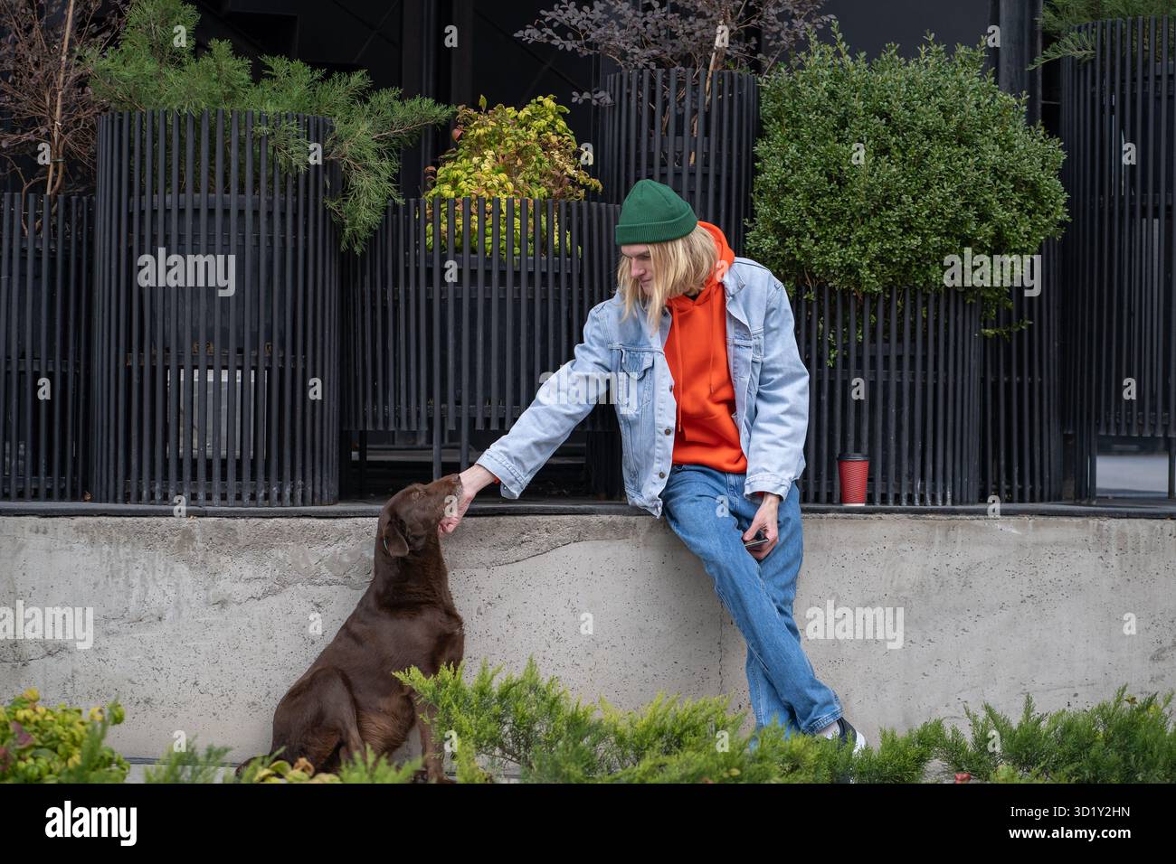 Netter, stylischer Hipster-Typ im trendigen Outfit, streichelt Straßenhund, spielt, amüsantes, obdachloses Haustier Stockfoto
