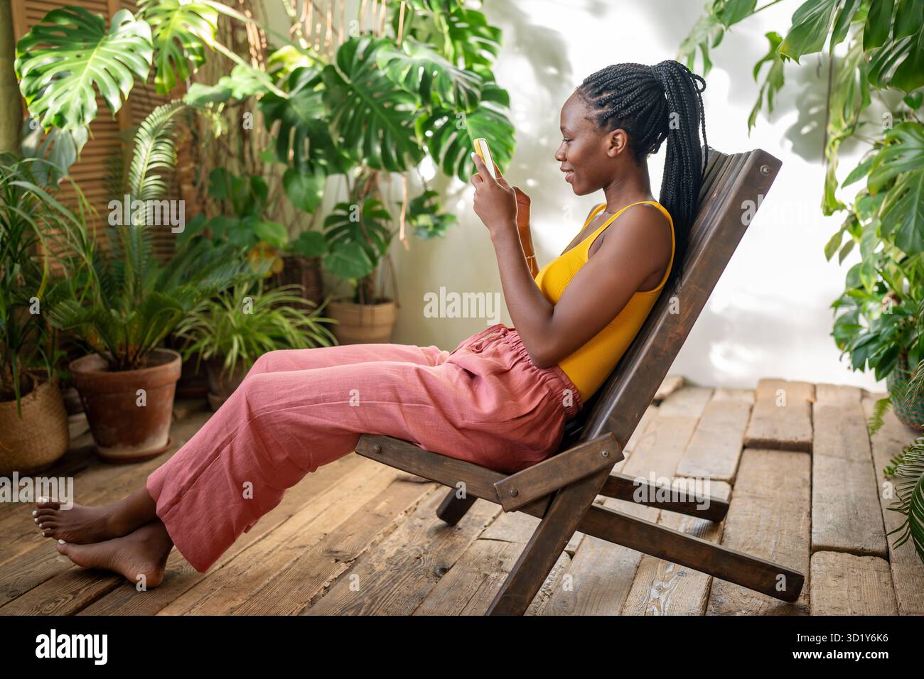 Kichernde Afroamerikanerin mit Telefon. Glückliches Mädchen, das sich im urbanen Dschungel zu Hause entspannt. Stockfoto