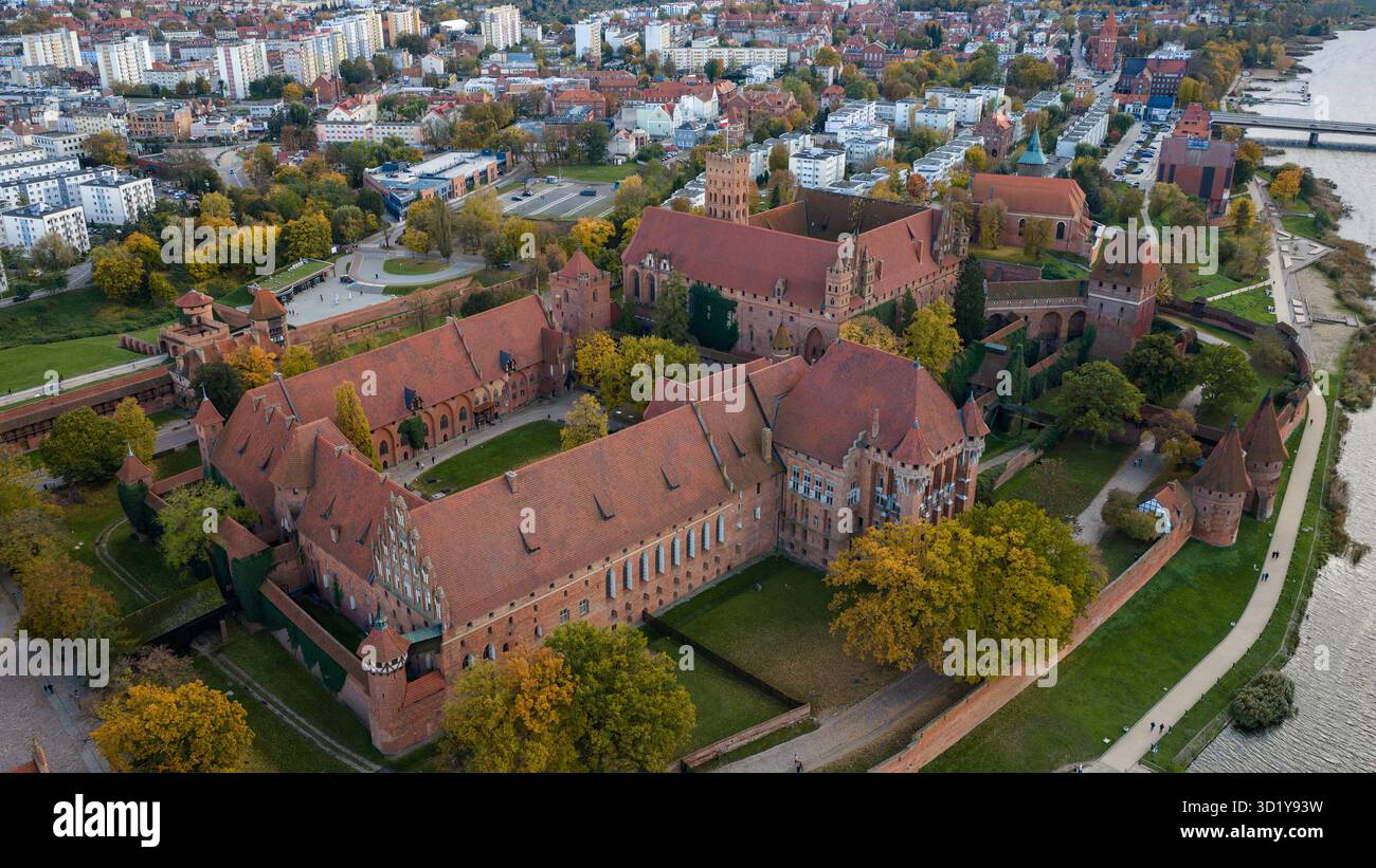 Die Drohnenansicht zeigt die Burg Malbork in Nordpolen, rote Backsteinmauern, Türme, Innenhöfe und Dächer entlang des Flusses Nogat mit Herbstbäumen Stockfoto