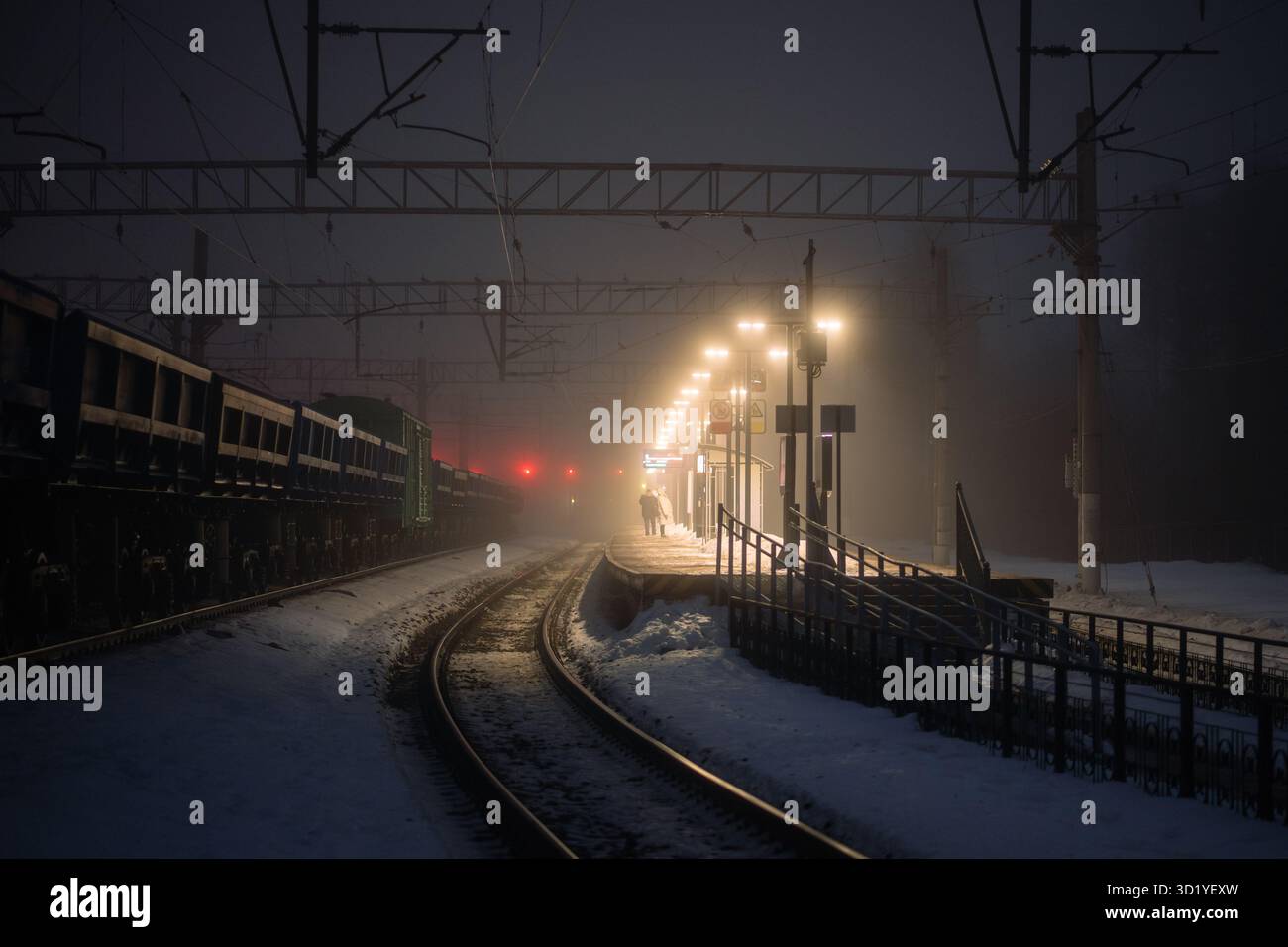 Zwei Personen auf einem nebeligen Bahnsteig überprüfen den Zeitplan, warten auf verspätete Züge bei nachträglicher Schneesturm-Nebel-Kälte Stockfoto