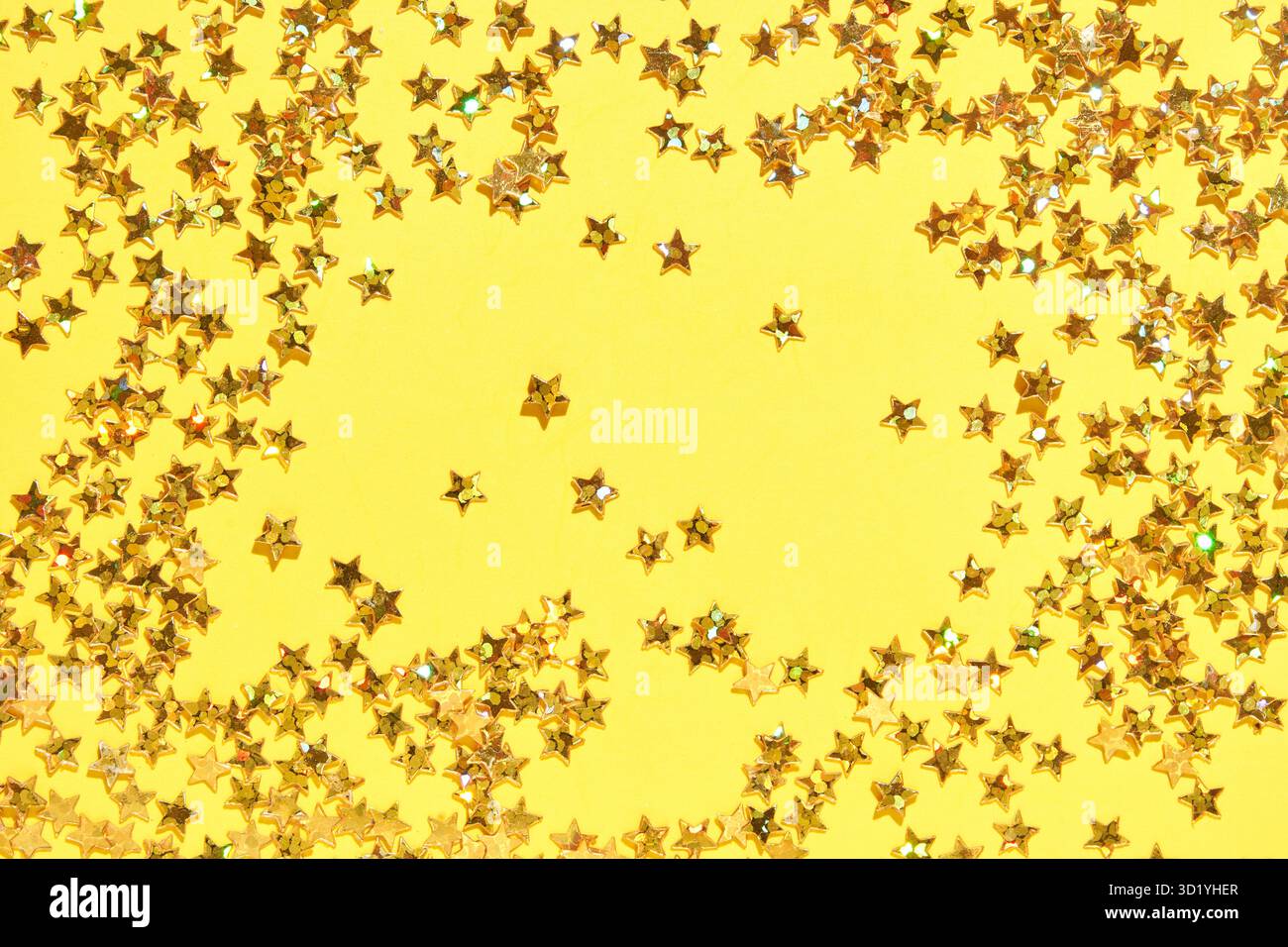 Funkelndes Goldsternkonfetti auf gelbem Hintergrund für festliche und festliche Themen. Stockfoto