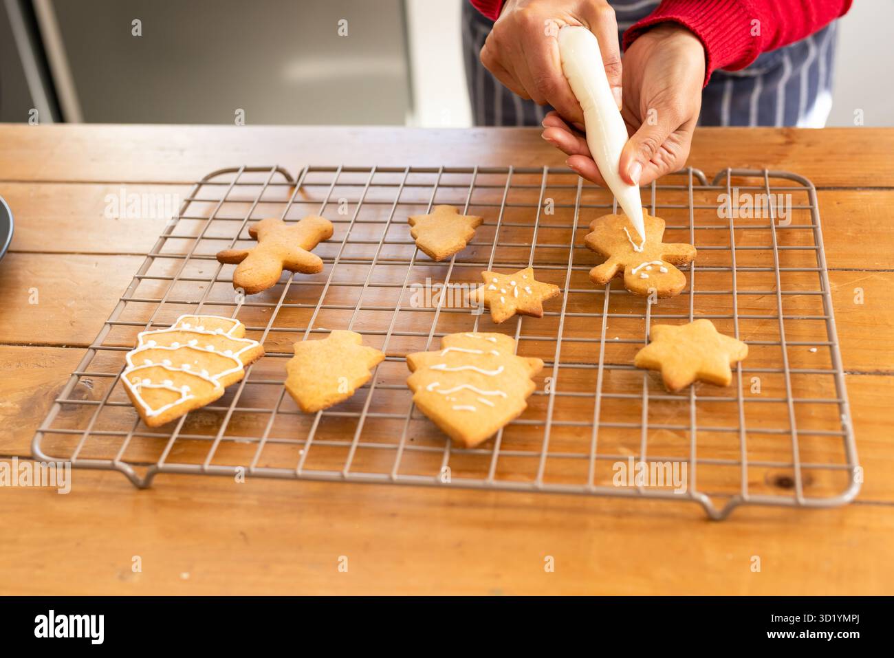Weiße Glasur wird auf Lebkuchenmann-Kekse auf hölzernen Tischplatten mit verschiedenen Eiskeksen gegossen Stockfoto