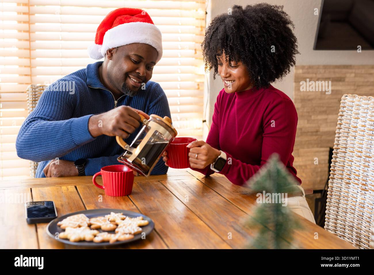 Diverse Paare, die Kaffee aus der französischen Presse in die Tassen in der Ecke mit Weihnachtskeksen gießen Stockfoto