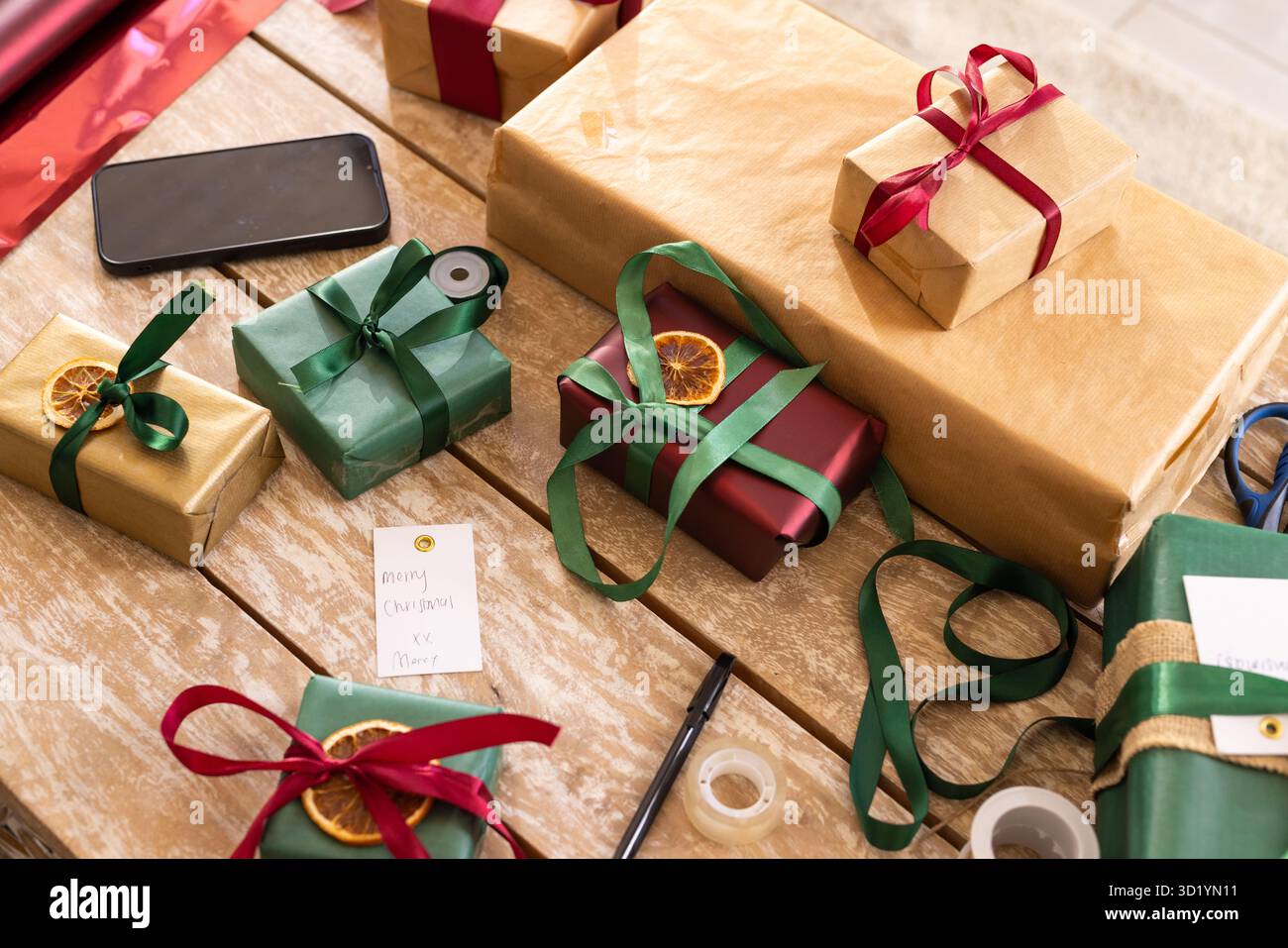 Gewickelte Geschenke liegen auf einer Holzplatte mit Band, Schere und handgeschriebenem Geschenkanhänger Stockfoto