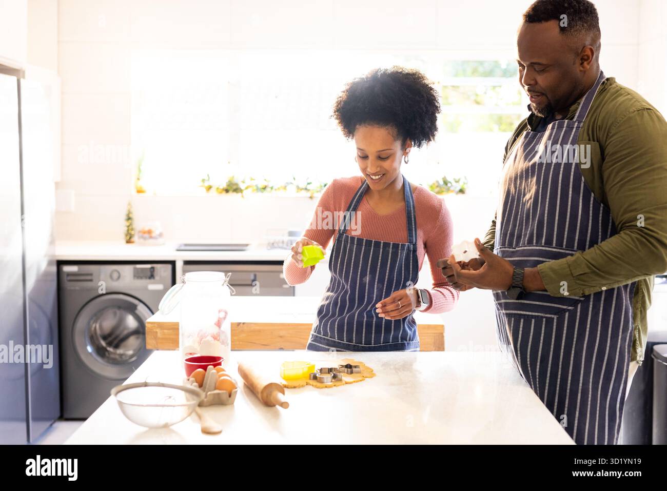 Diverse Paare in Schürzen schneiden Keksteig mit Nudelnadel und Keksschneider auf Kücheninsel Stockfoto