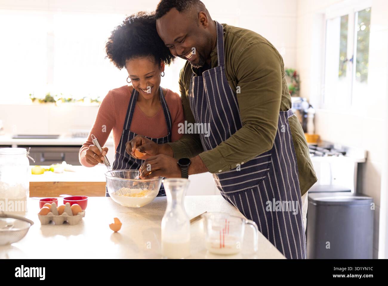 Diverse Paare, die gestreifte Schürzen tragen, Eier knacken und auf der Kücheninsel mit einer Rührschüssel rührten. Kochen, kulinarisch, einheimisch, Lifestyle, Minimalis Stockfoto