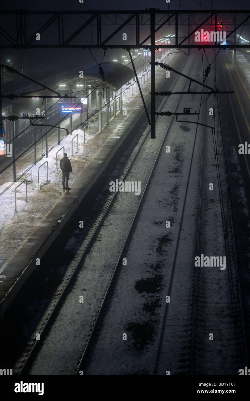 Single Mann steht auf Zug unter winterlichem Nachthimmel, Nebel mit kalter Feuchtigkeit. Alleinfahrt, verspäteter Zug Stockfoto