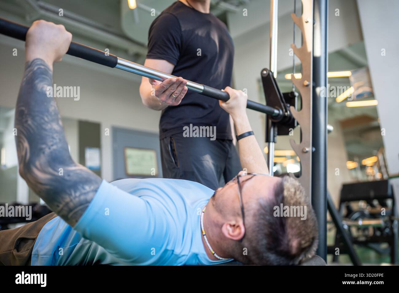 Kräftiger muskulöser Athlet, der die Langhantel im Fitnessstudio hebt, mit professioneller Personal Trainer-Unterstützung beim Workout Stockfoto