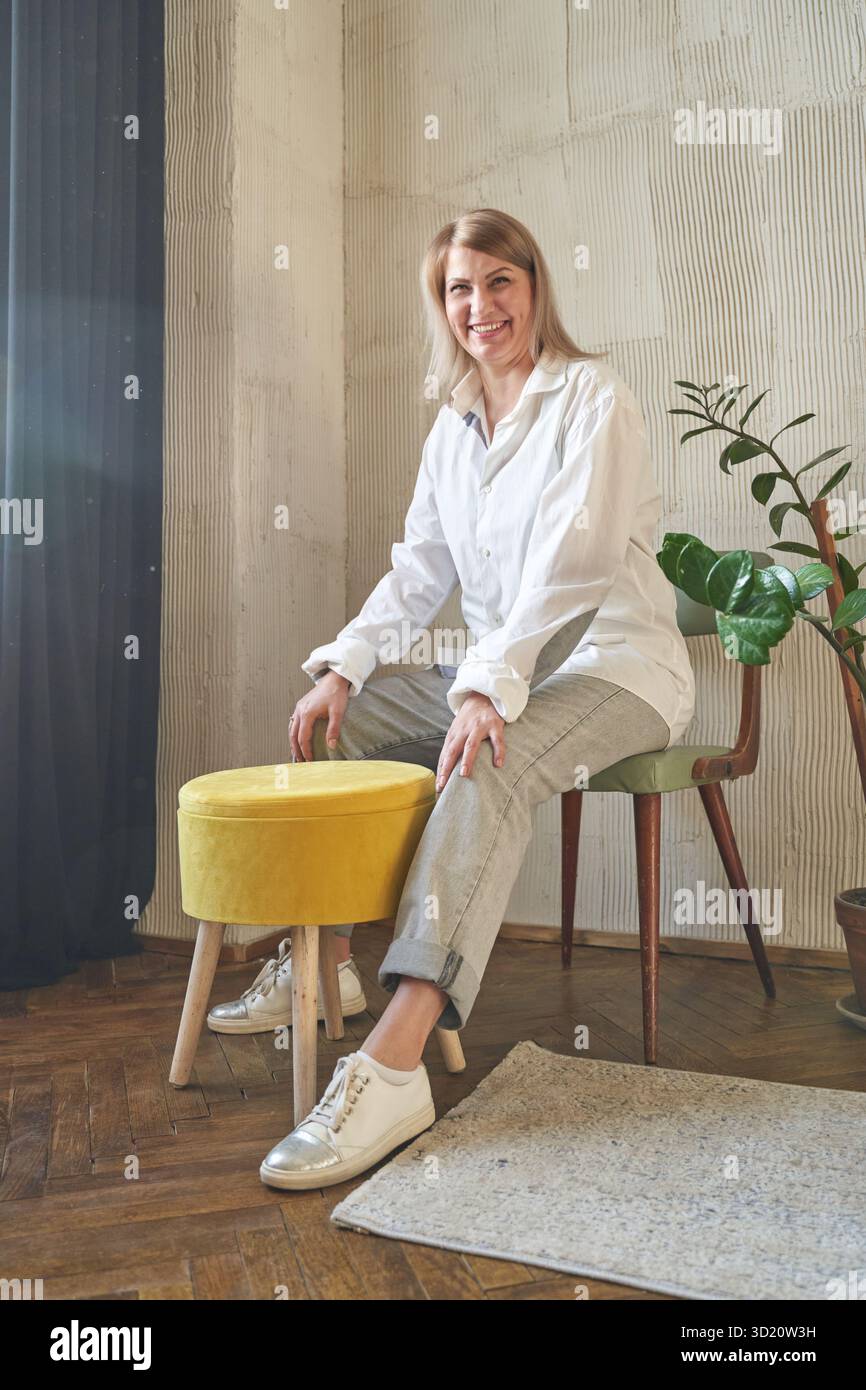 Reife weiße Frau in lässiger Kleidung, die drinnen mit Pflanzen und rustikal sitzt Stockfoto