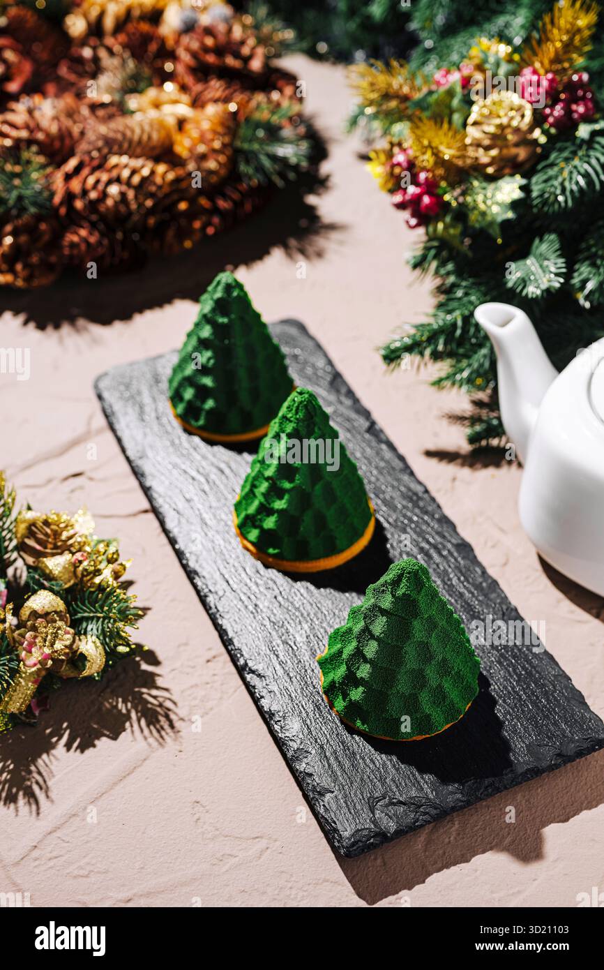 Weihnachtsdessert mit festlichem grünen konischen Gebäck und einer Teekanne auf einem rustikalen Tisch Stockfoto