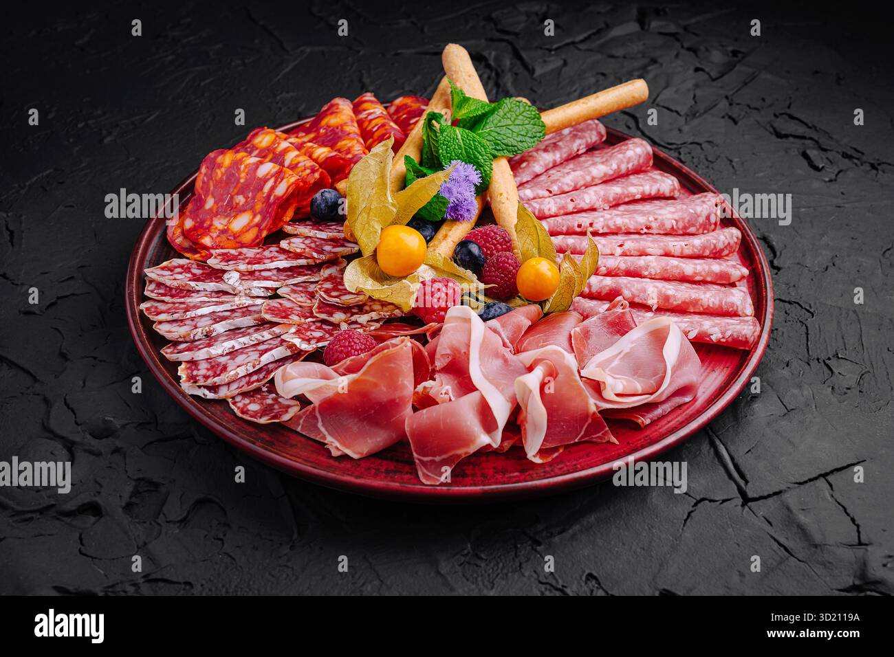 Räucherfleisch und Obst sind wunderschön auf einer dunklen Platte für eine Gourmet-Präsentation angeordnet Stockfoto