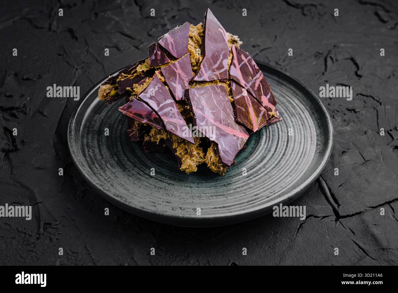 Farbenfrohes Dubai Schokoladendessert mit auffälligen lila Mustern, serviert auf einem dunklen Teller in modernem Ambiente Stockfoto