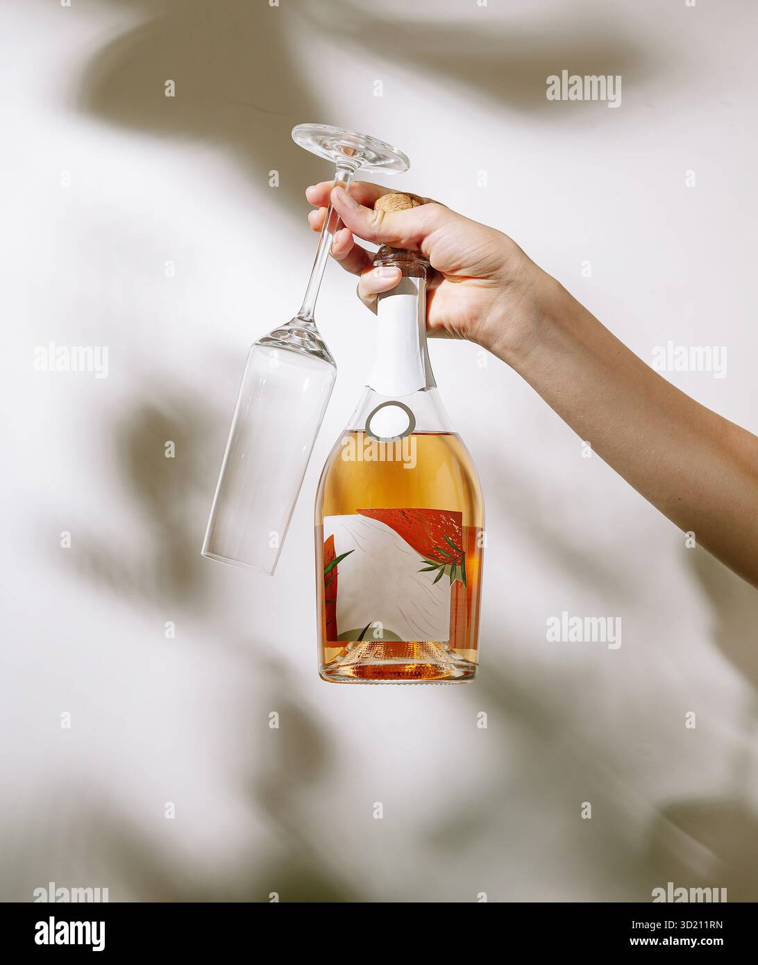 Hand mit einer Flasche Rosenwein und einem leeren Glas mit Blumenetikett in sanfter Beleuchtung Stockfoto