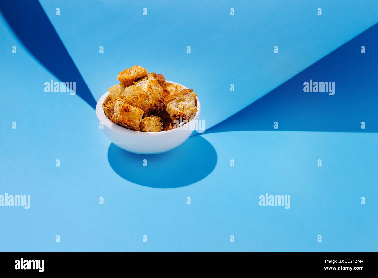 Goldene knusprige Brotwürfel in einer weißen Schüssel vor blauem Hintergrund schaffen einen optisch ansprechenden Kontrast Stockfoto