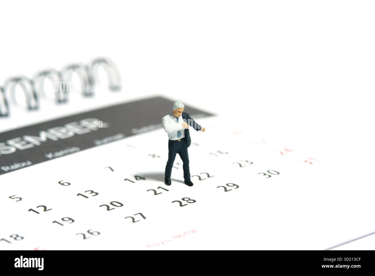 Miniatur-Kleinkinder-Spielfiguren-Fotografie. Ein Geschäftsmann, der sich mit Anzug über dem Kalender fertig macht. Isoliert auf weißem Hintergrund. Bild-ph Stockfoto
