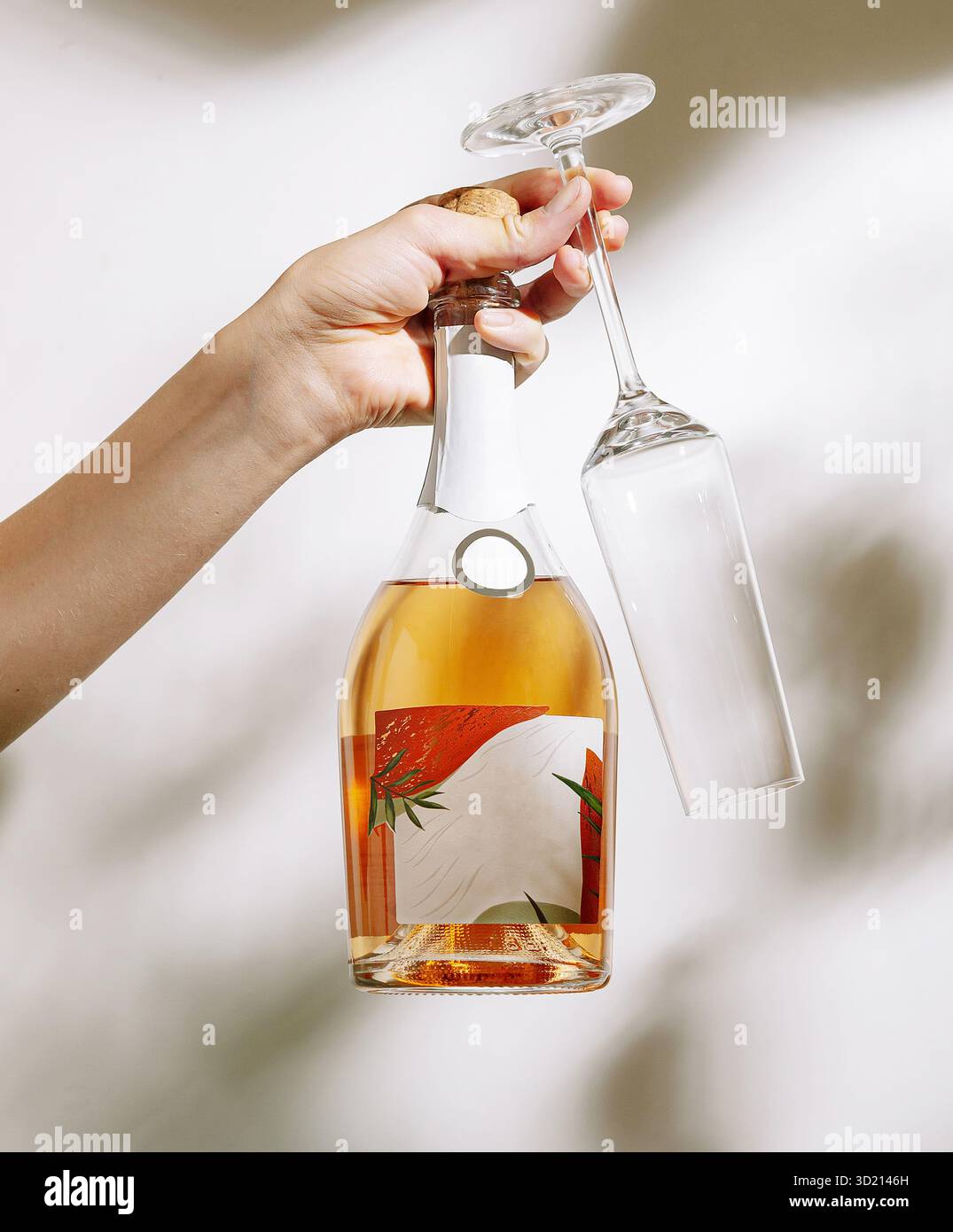 Hand mit einer Flasche Rosenwein und einem leeren Glas mit Blumenetikett in sanfter Beleuchtung Stockfoto