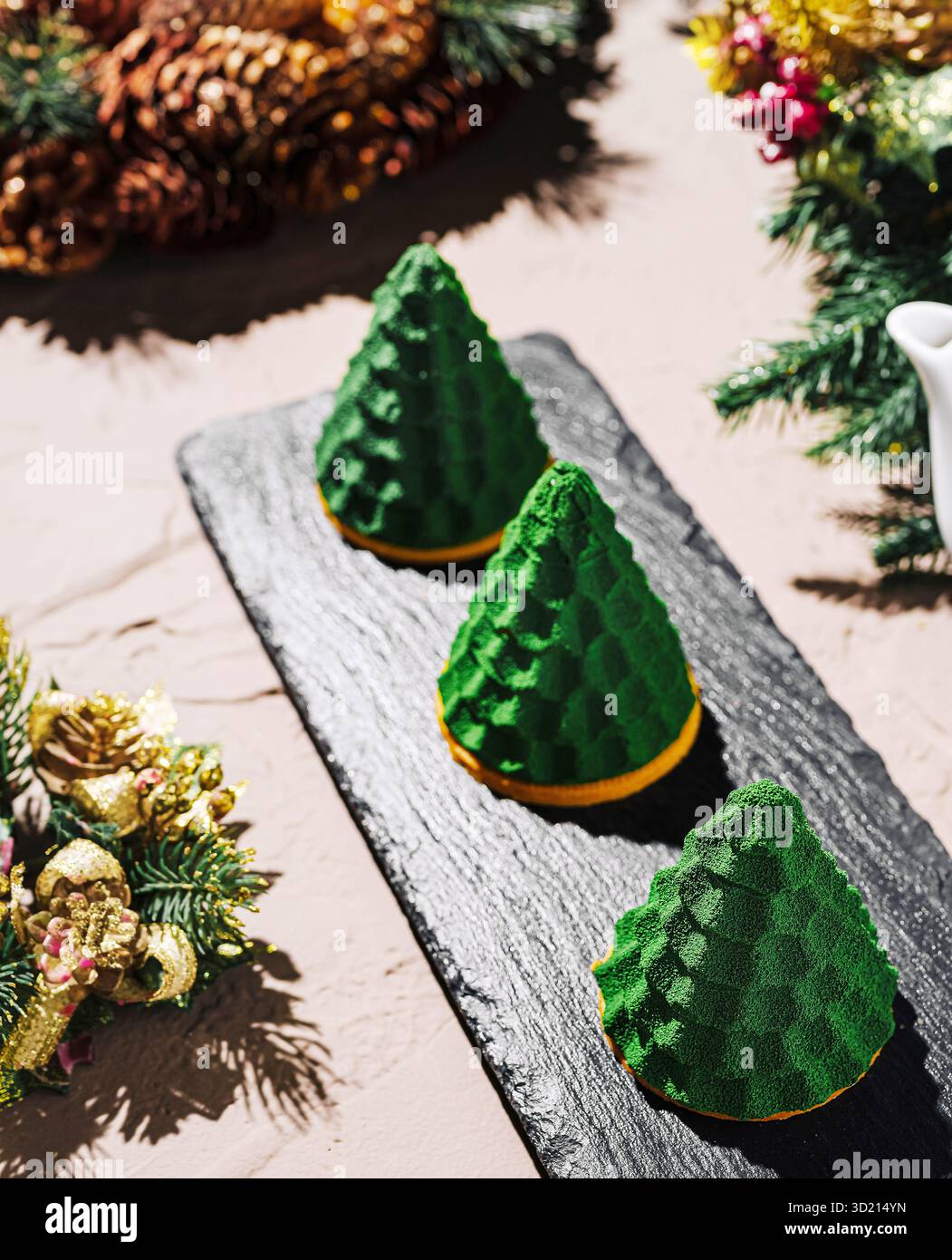 Weihnachtsdessert mit festlichem grünen konischen Gebäck und einer Teekanne auf einem rustikalen Tisch Stockfoto