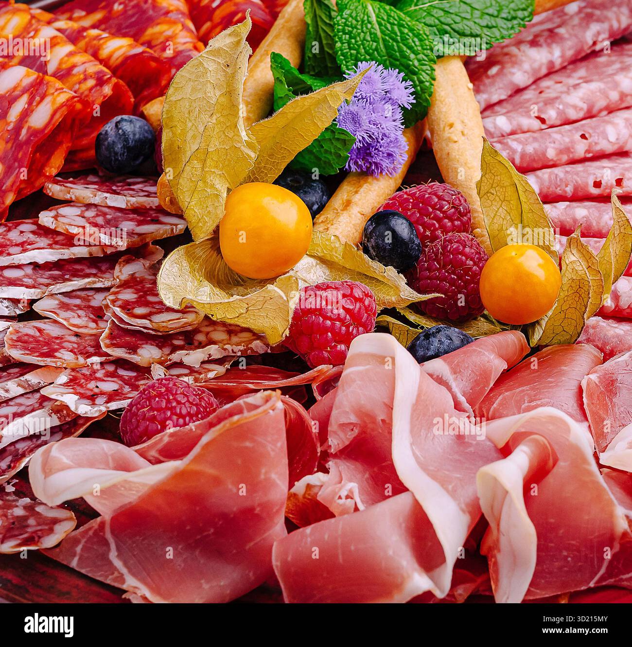 Räucherfleisch und Obst sind wunderschön auf einer dunklen Platte für eine Gourmet-Präsentation angeordnet Stockfoto