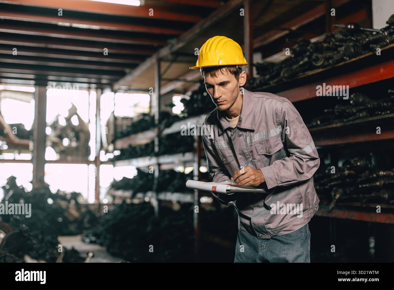 Techniker männliche Arbeiter prüfen den Bestand im Lager alter Gebrauchtmaschinenteile mit Schutzhelm. Stockfoto