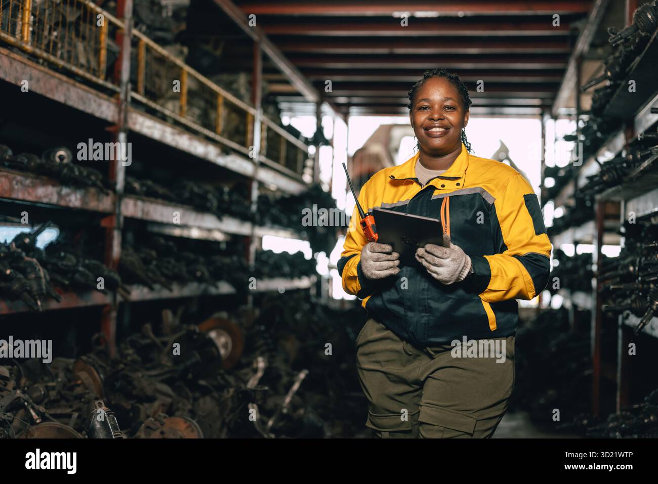Glückliche schwarze afrikanische Ingenieurinnen arbeiten gerne in alten Lagerlagern für gebrauchte Metallmaschinenteile. Stockfoto