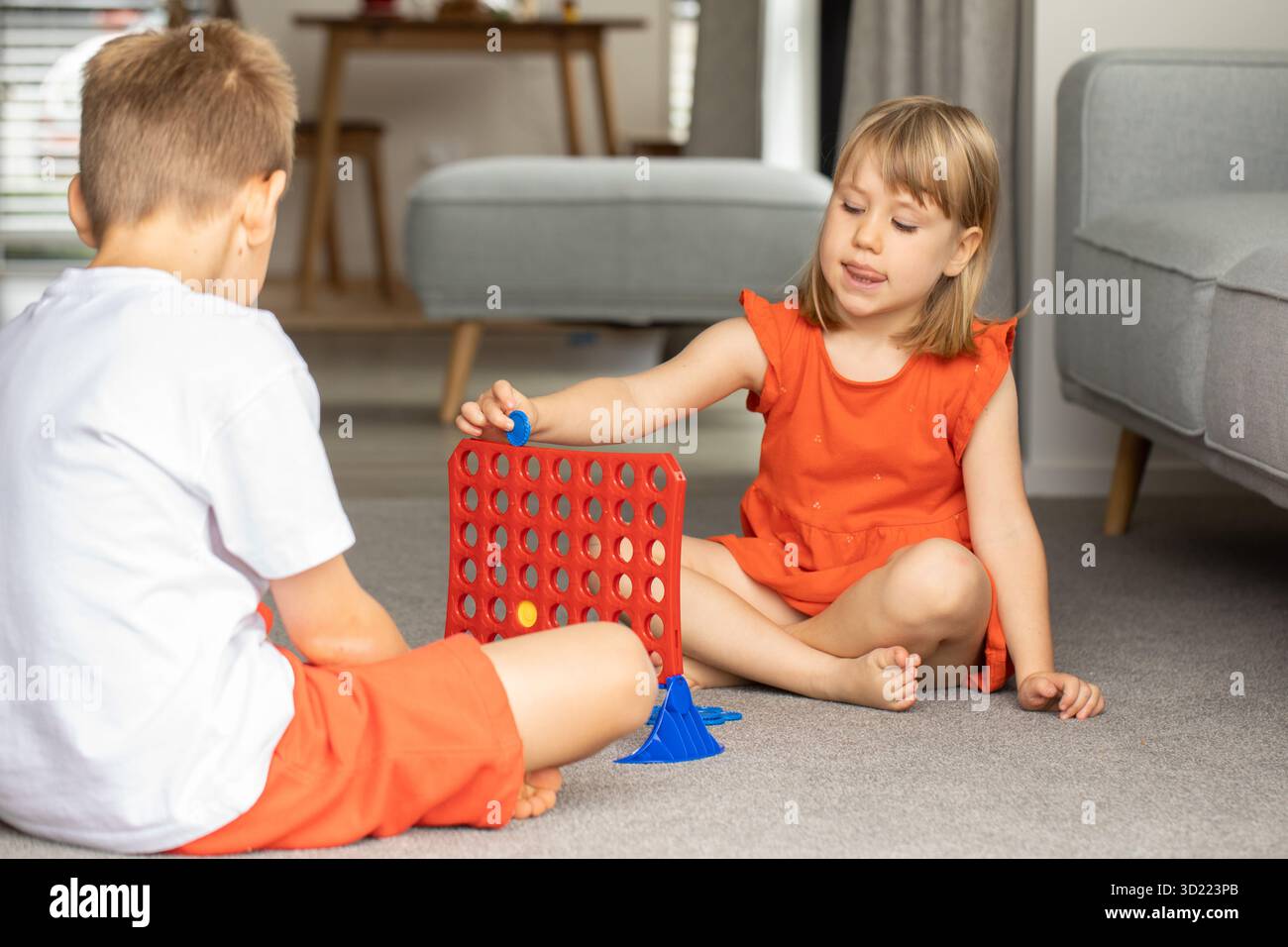 Geschwister, die in ein strategisches Brettspiel vertieft sind und ihre Logik verbessern. Kinder spielen Brettspiele - vier in einer Reihe Stockfoto