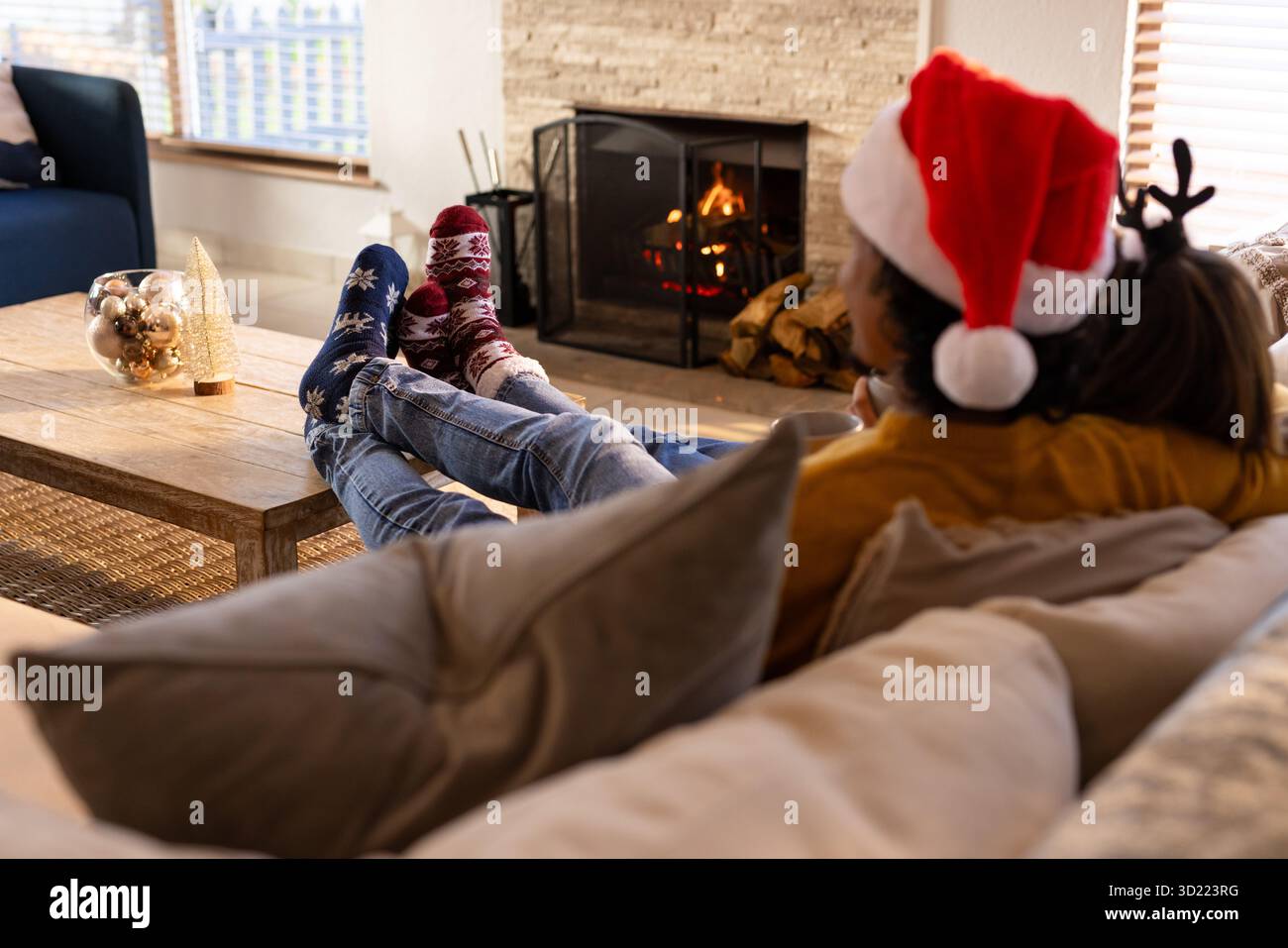 Ein Paar, das sich auf der Couch im Wohnzimmer mit Weihnachtsmütze und festlichen Socken am Kamin liegend Stockfoto