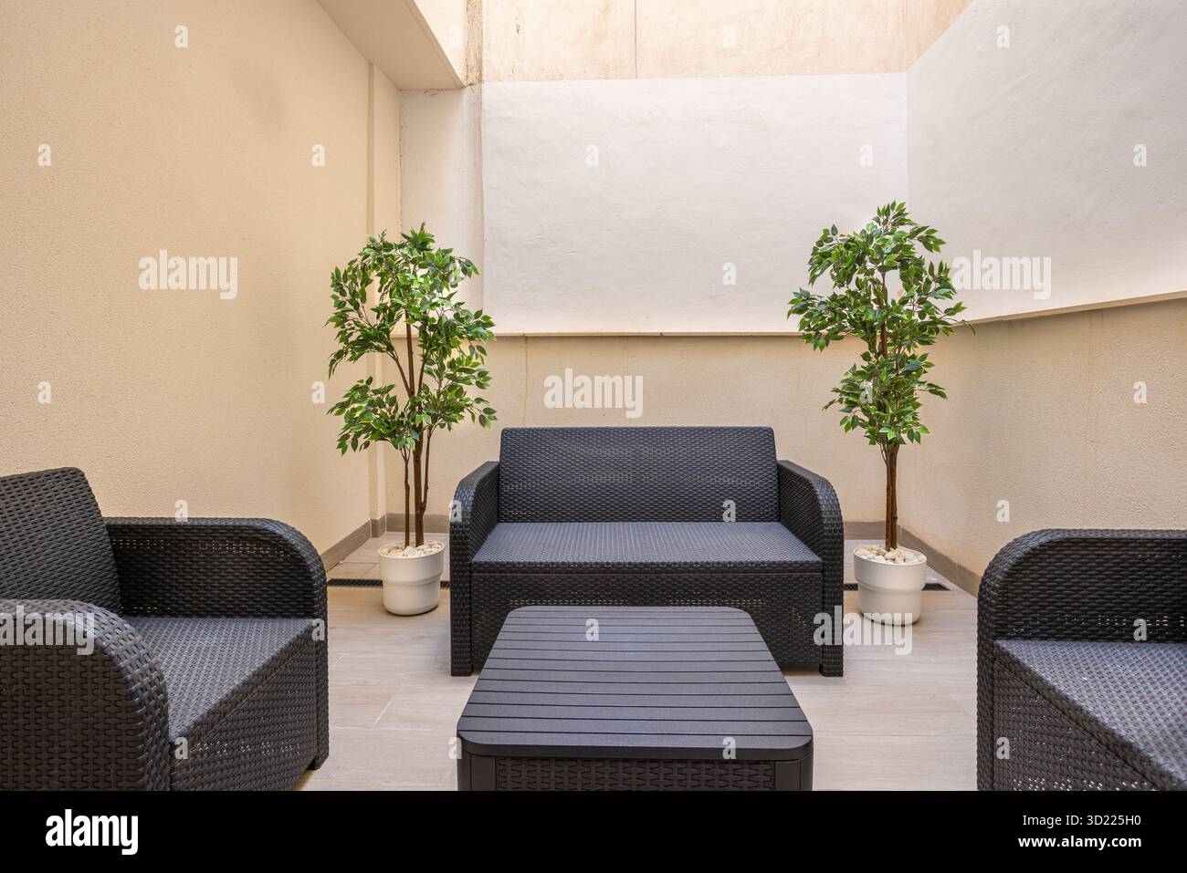 Gemütliche private Terrasse mit schwarzen Webmöbeln und grünen Topfpflanzen in Eckbereichen Stockfoto