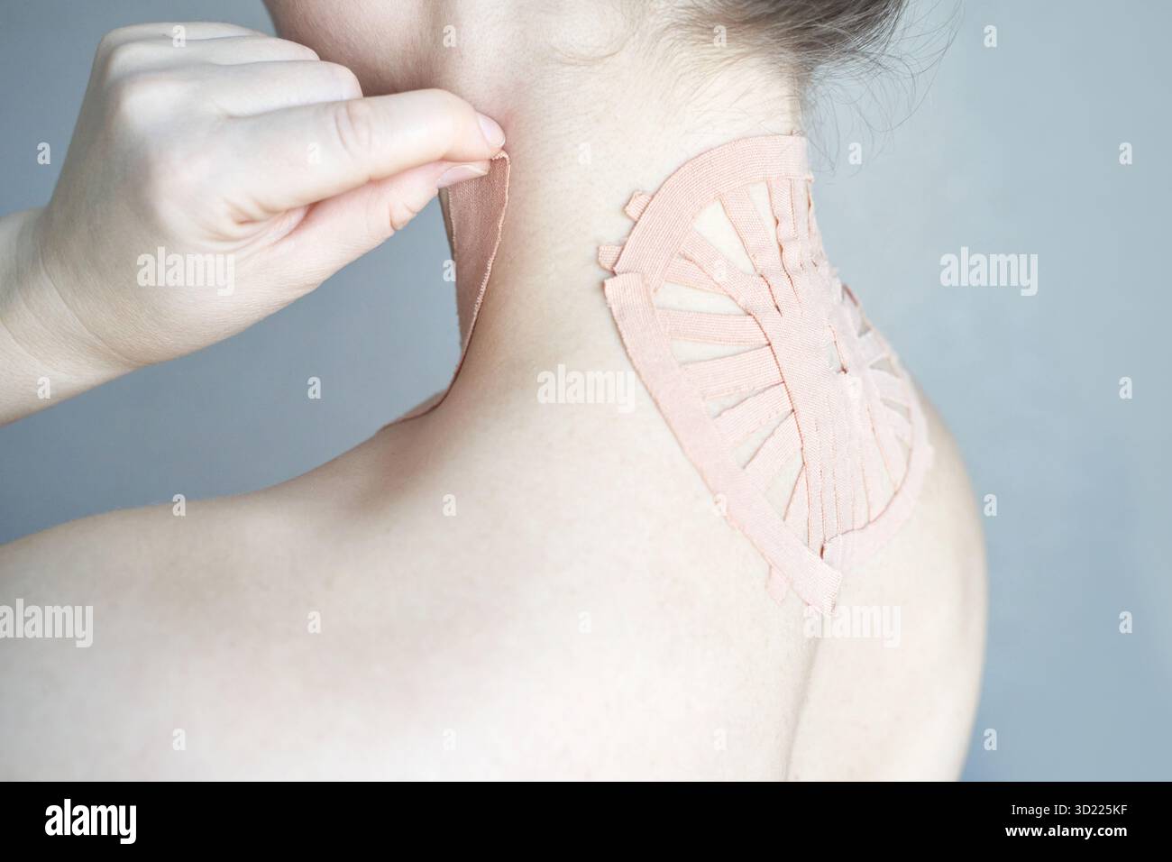 Weibliche Anwendung von therapeutischem Klebeband am oberen Rücken zur Schmerzlinderung und Haltung Stockfoto