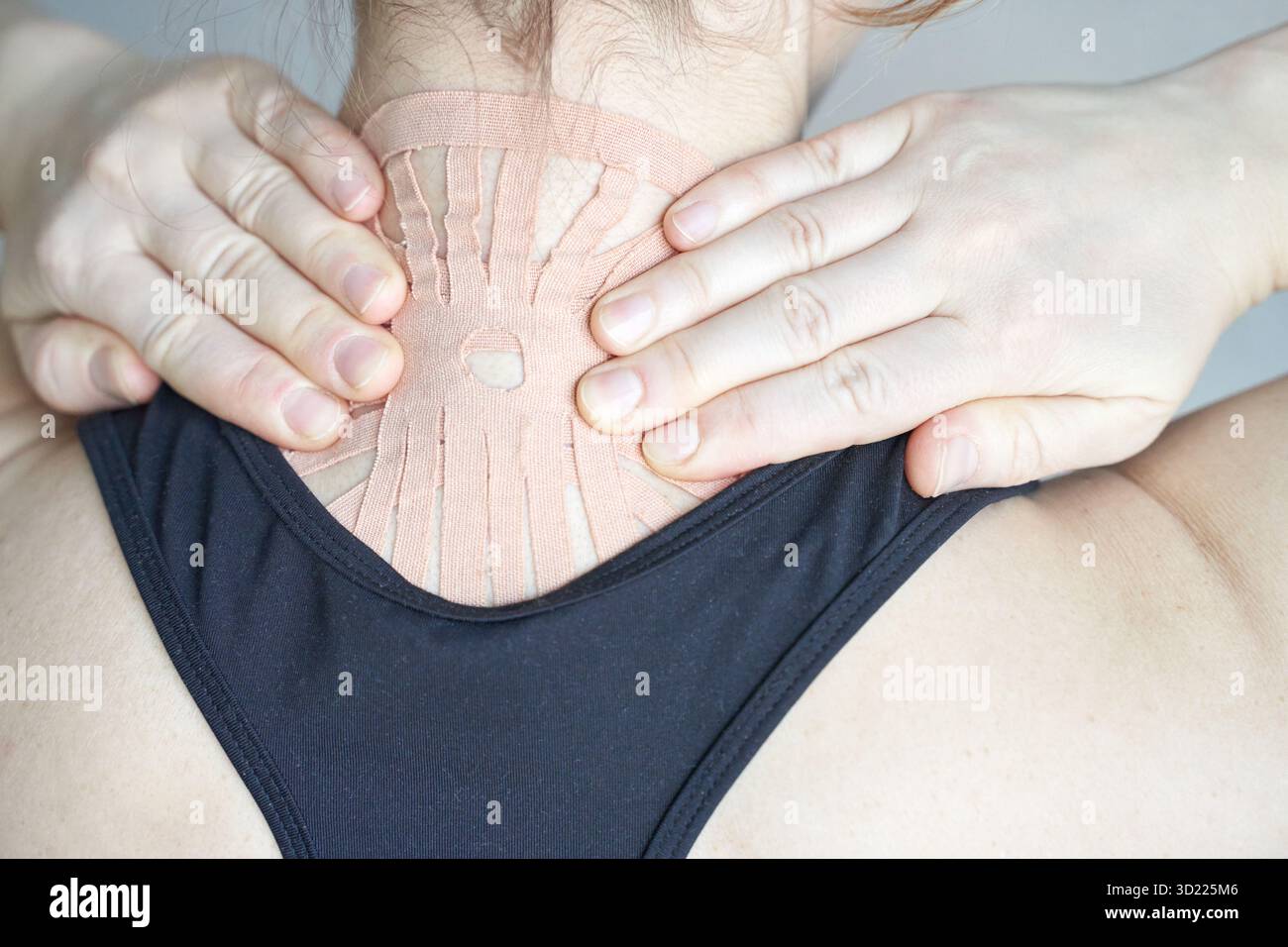 Junge kaukasische Frau, die zur Schmerzlinderung therapeutisches Klebeband am Hals aufträgt Stockfoto