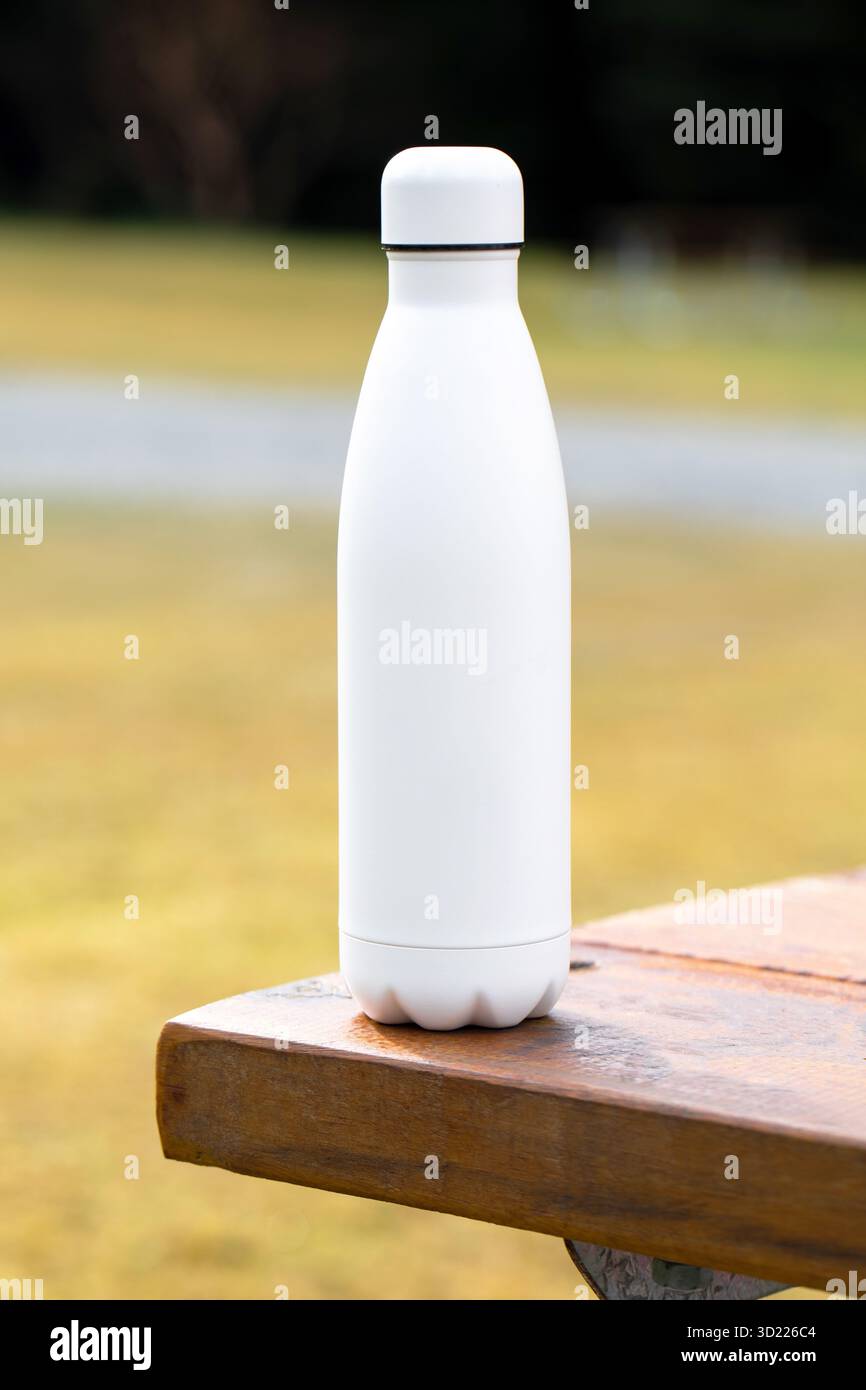 Leere Thermoskanne auf Holztisch in der Nähe des Landes. Nachfüllbare Wasserflasche mit Modellschablone auf rustikaler Arbeitsfläche. Stockfoto