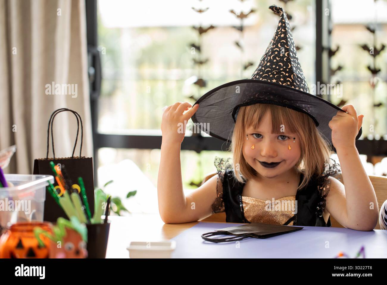 Halloween-Party für Kinder. Ein Mädchen im Hexenkostüm bastelt an Halloween ein Haus Stockfoto