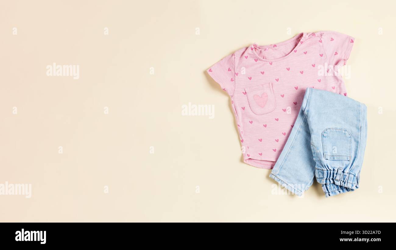 Pinkes Kinder-T-Shirt und gefaltete Jeans auf beigefarbenem Hintergrund. Modischer Casual-Look für ein Mädchen. Speicherplatz kopieren. Stockfoto