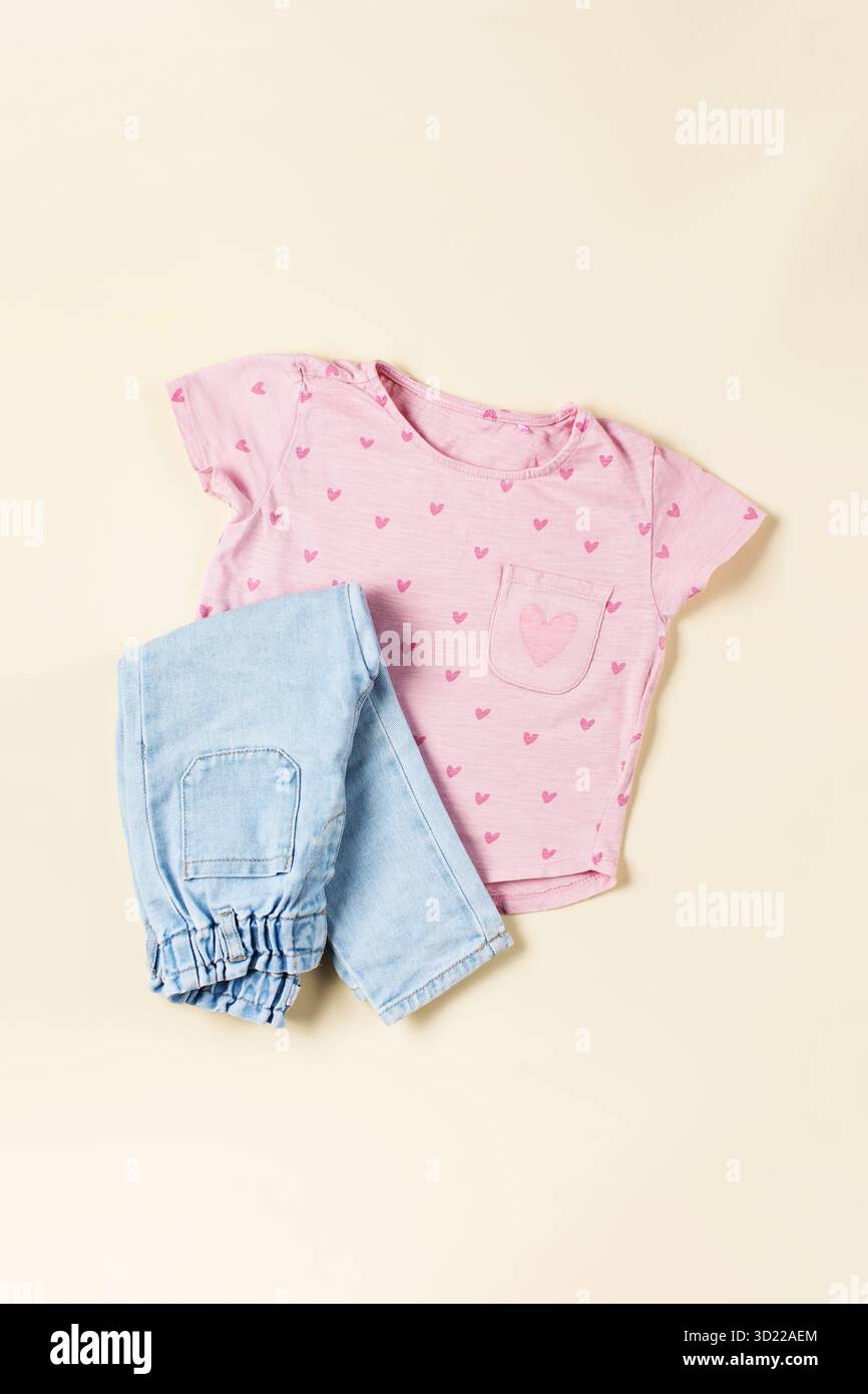Pinkes Kinder-T-Shirt und gefaltete Jeans auf beigefarbenem Hintergrund. Modischer Casual-Look für ein Mädchen. Stockfoto