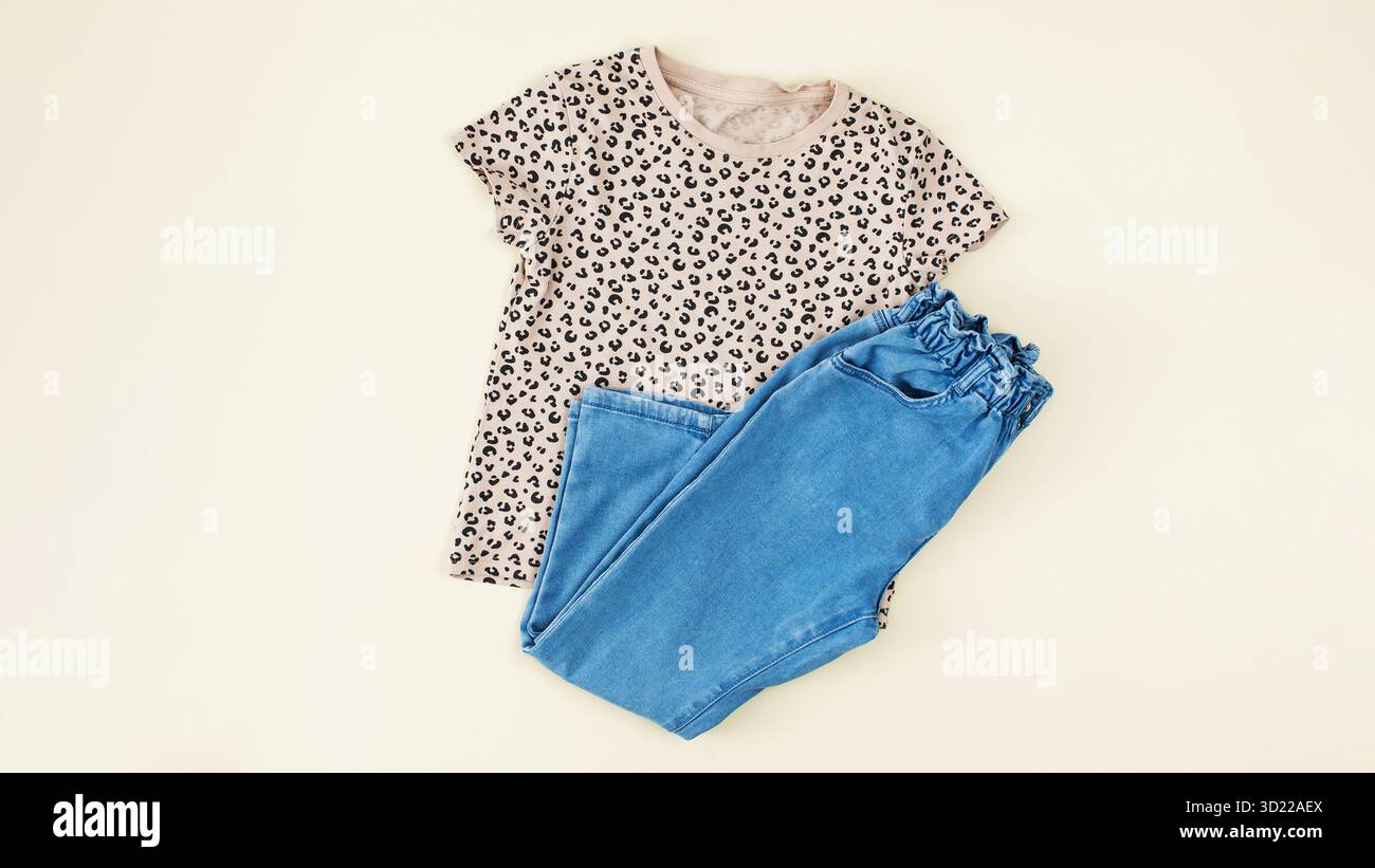 Ein Set stilvoller Kleidung für Kinder. Jeans und ein T-Shirt auf beigefarbenem Hintergrund für ein Mädchen. Stockfoto