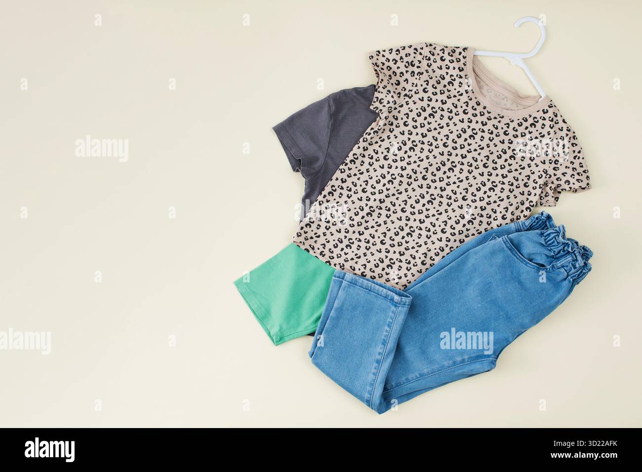 Ein Set stilvoller Kleidung für Kinder. Jeans und ein T-Shirt auf beigefarbenem Hintergrund für ein Mädchen. Stockfoto