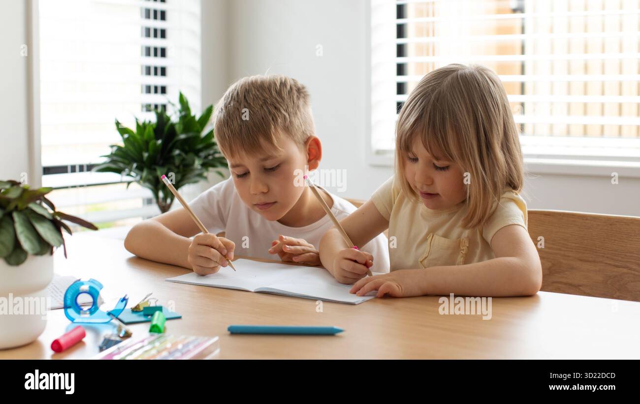 Bruder und Schwester schreiben und zeichnen zusammen mit Bleistiften am Tisch. Das Konzept der Heimschulung Stockfoto