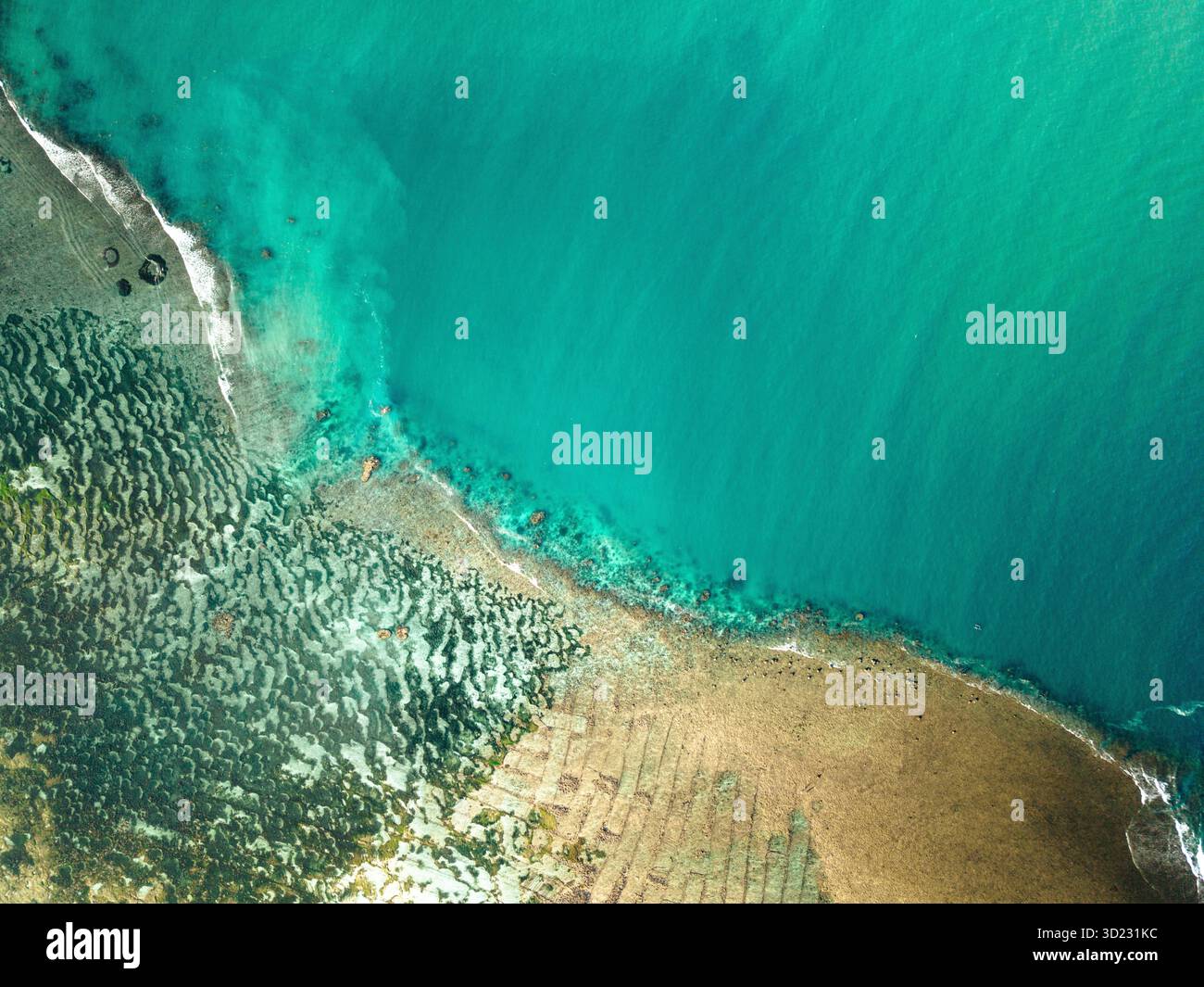 Aus der Vogelperspektive auf eine pulsierende Küste mit türkisfarbenem Wasser, das auf eine strukturierte Küste trifft. Lombok, Gerupuk, Indonesien Stockfoto
