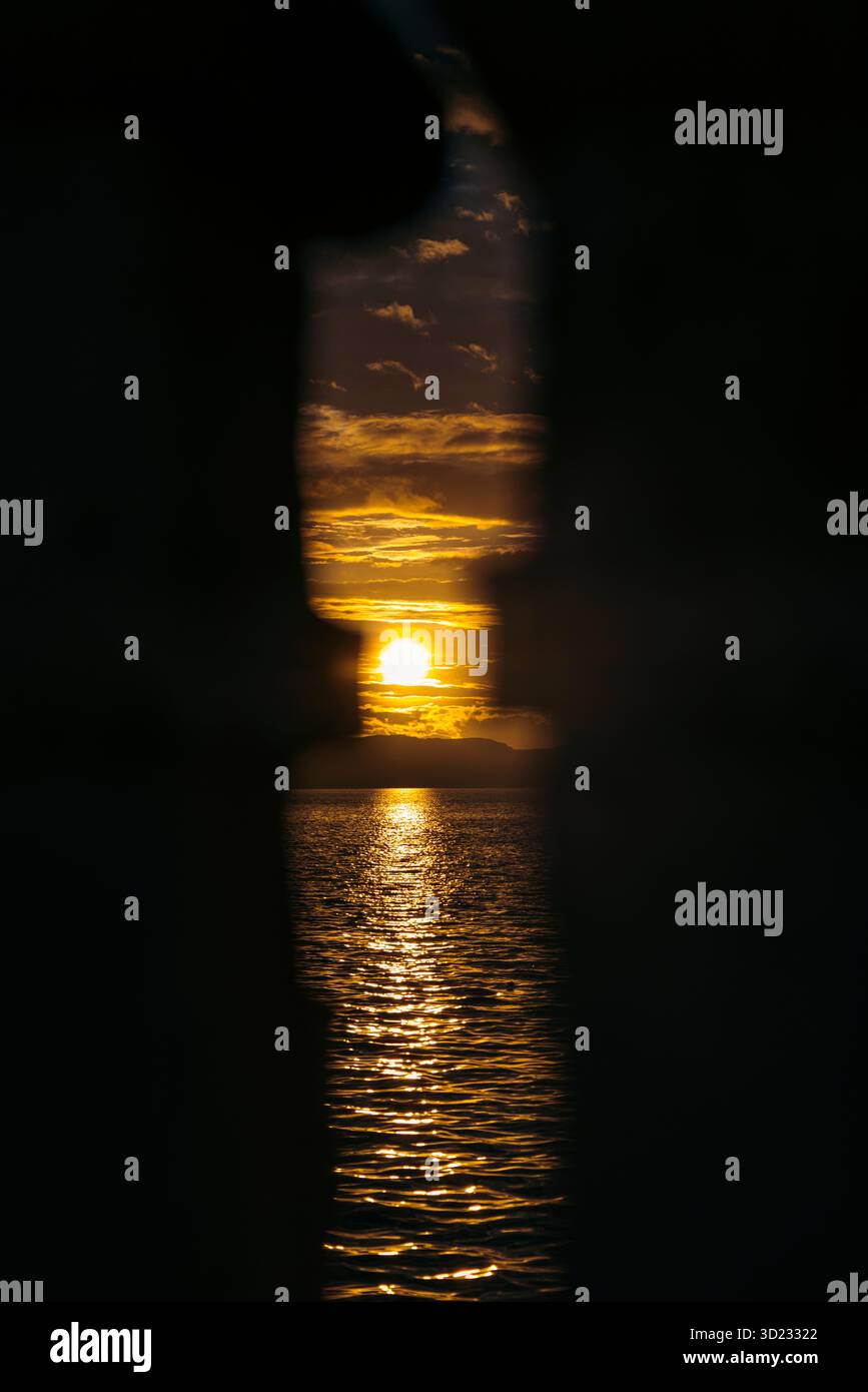 Lebendiger Sonnenuntergang über dem Ozean, eingerahmt von Silhouetten vertikaler Strukturen. Ambon, Maluku, Indonesien Stockfoto