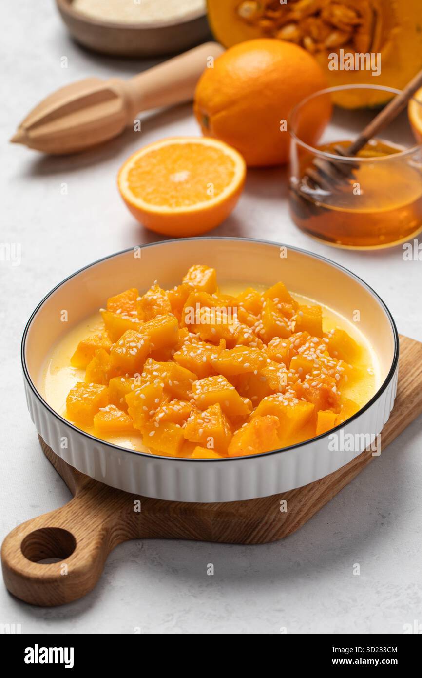 Schüssel mit frisch gewürfeltem Kürbis mit Sesam und Zitrusfrüchten auf Holzbrett Stockfoto