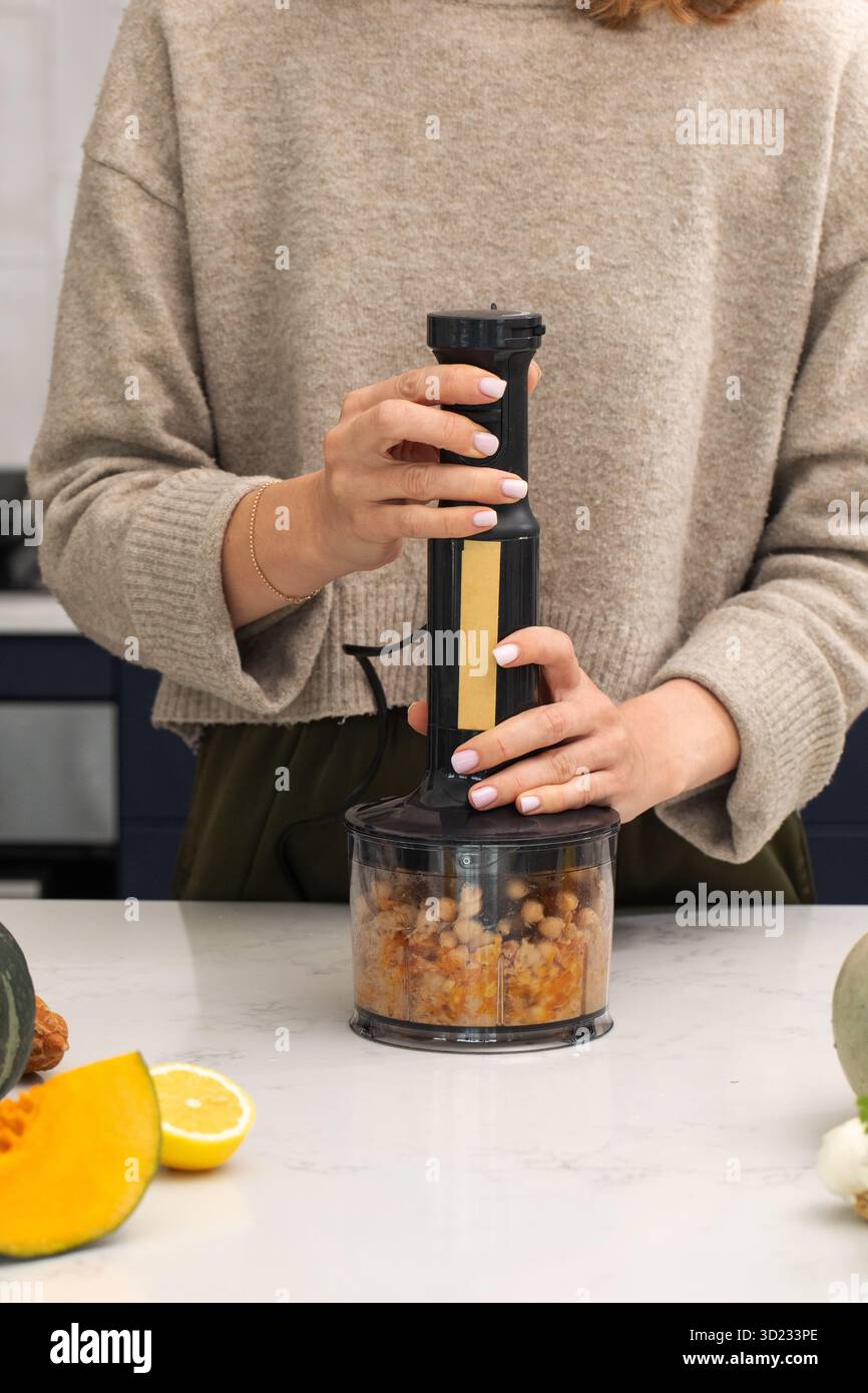 Frau, die den Stabmixer in der Küche für eine gesunde Mahlzeit verwendet. Veganes Essen Stockfoto
