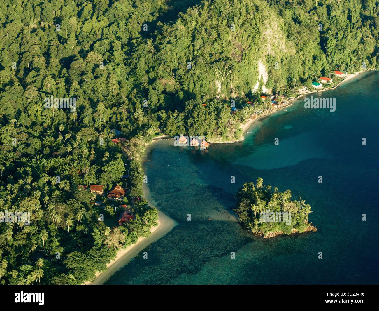 Blick aus der Vogelperspektive auf die üppige grüne tropische Küste mit ruhigem blauem Wasser und einem kleinen Küstendorf. Saleman Village, Seram Island, Indonesien Stockfoto