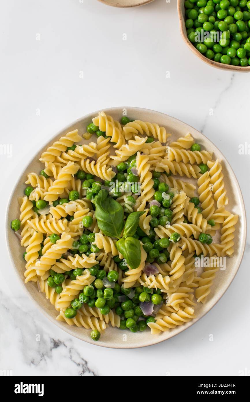 Vegetarische Pasta mit gekochten grünen Erbsen und Basilikum auf Teller Stockfoto