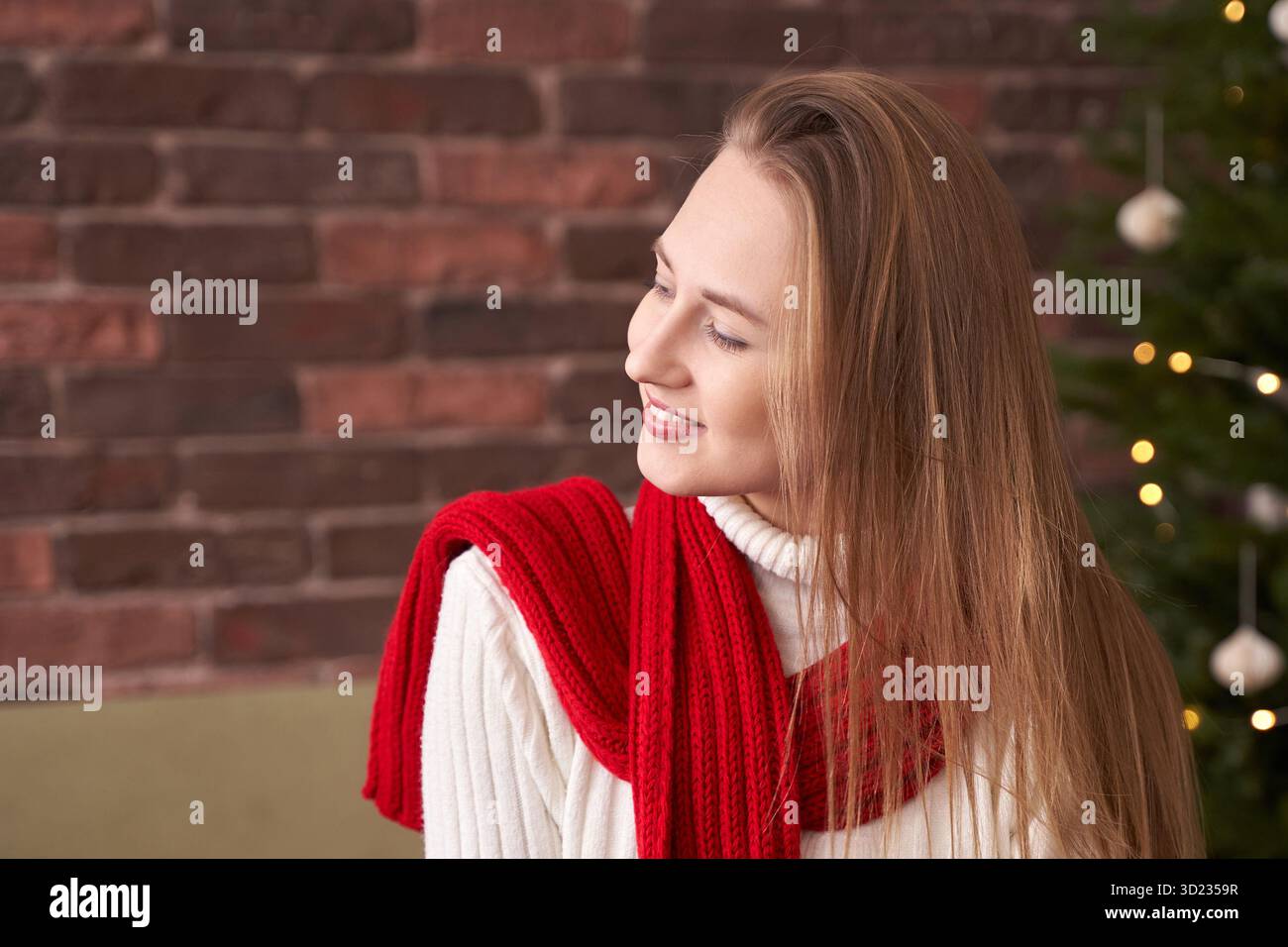 Kaukasische junge Frau im festlichen roten Schal lächelt neben dem verzierten weihnachtsbaum Stockfoto