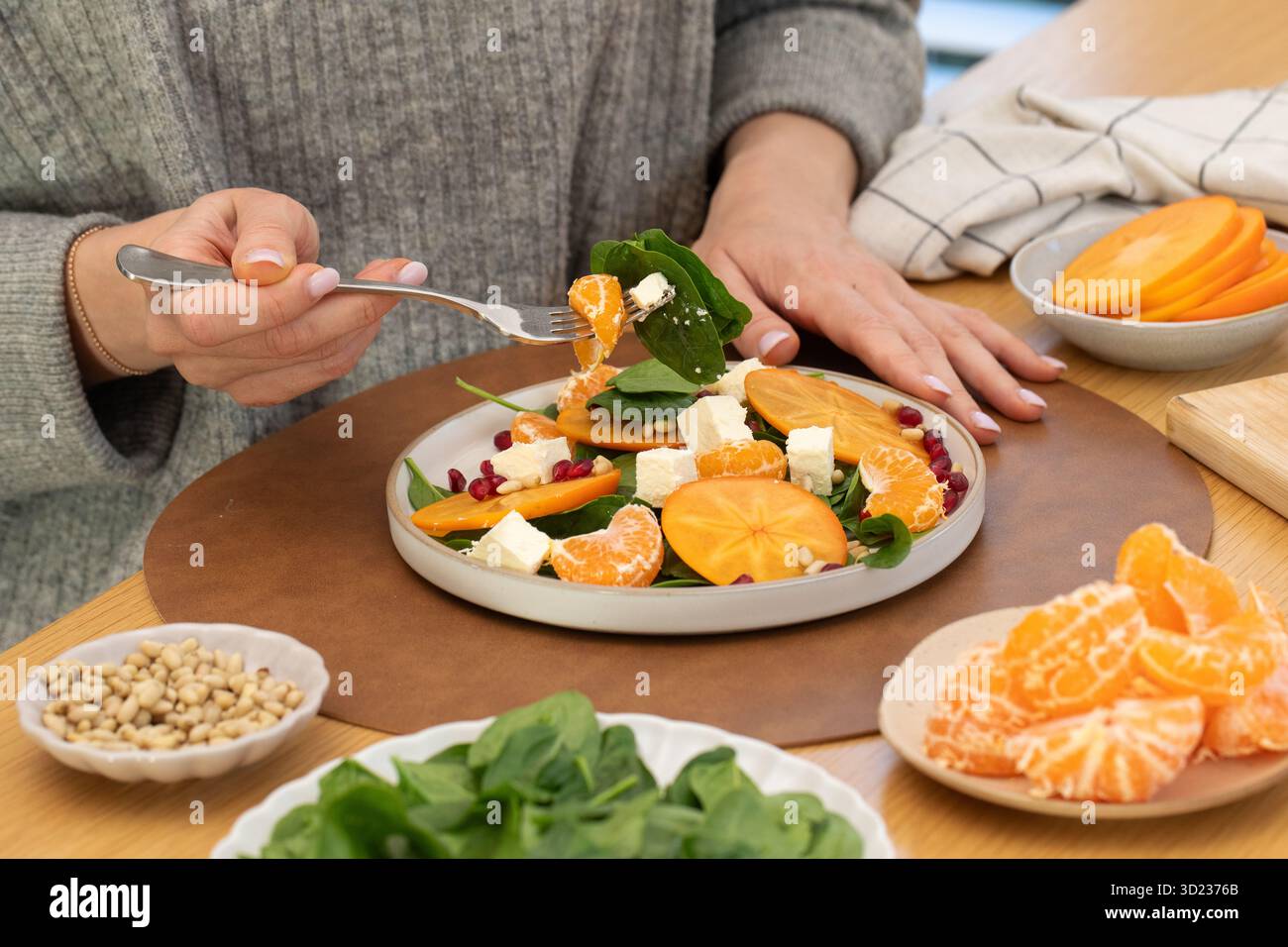 Frau, die gesunden Wintersalat mit Zitrusfrüchten, Persimmonen und Feta isst Stockfoto