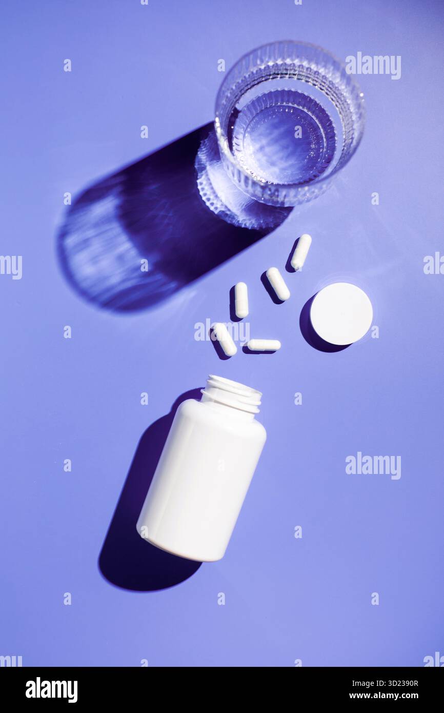 Ein weißes Gefäß, weiße Kapseln mit Vitaminen oder Arzneimitteln und ein Glas Wasser. Arzneimittel Stockfoto