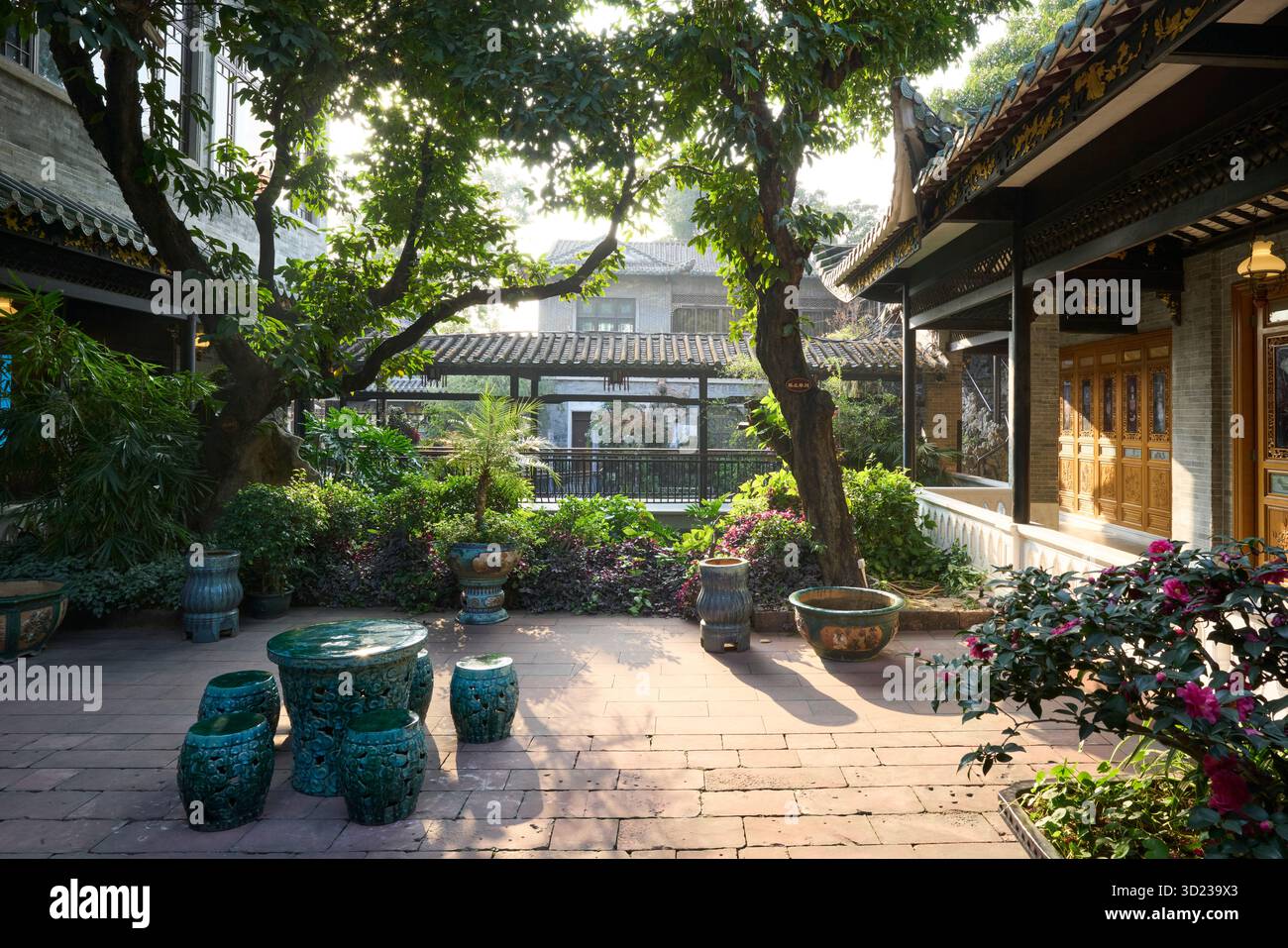 Guangzhou, China. Ein Innenhof im Bezirk Liwan, in der Nähe des Liwan Sees. Sonnendurchfluteter traditioneller Innenhof mit üppigem Grün und dekorativen Keramikhockern. Stockfoto