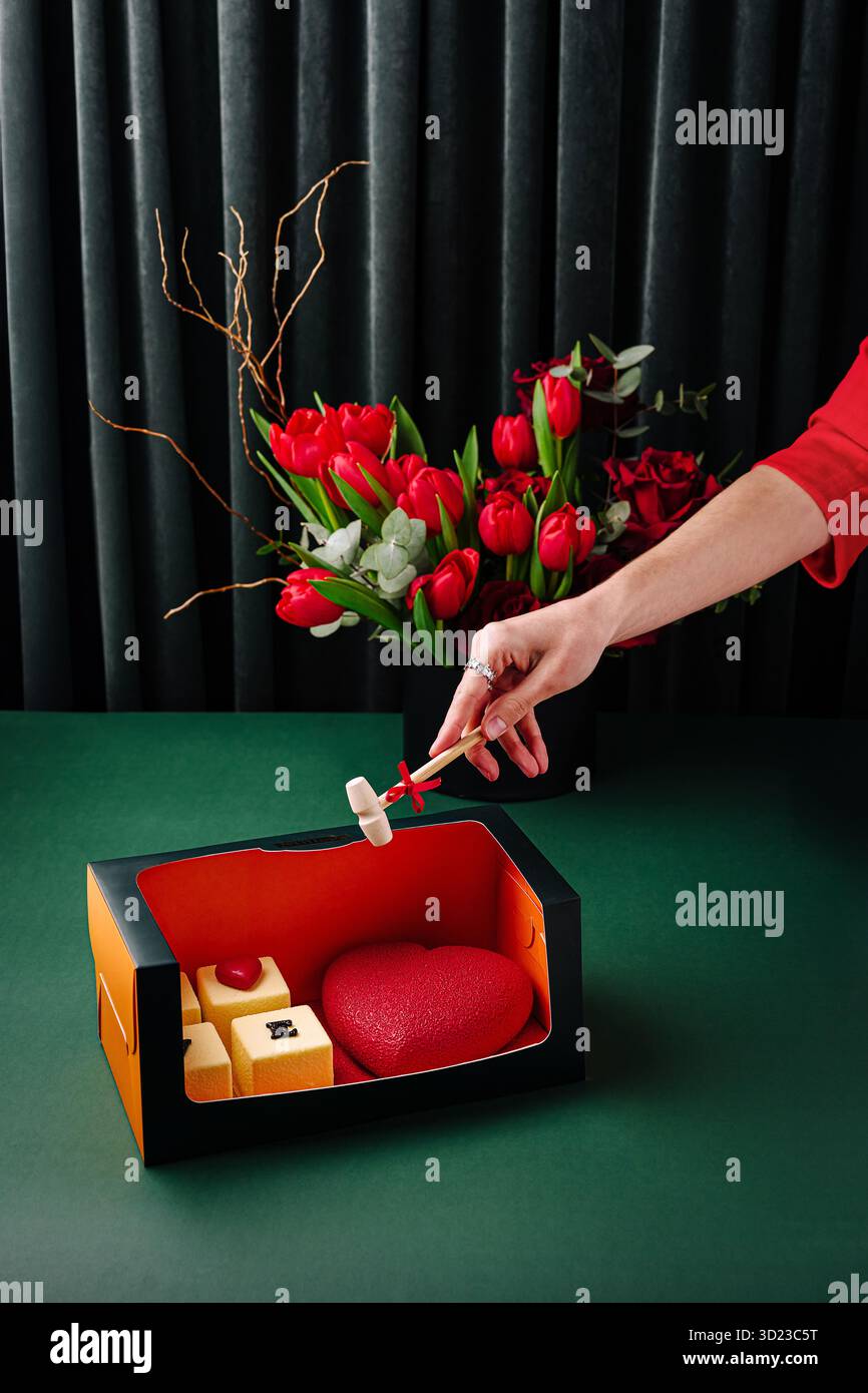 Eine luxuriöse Geschenkbox mit herzförmigen und würfelförmigen Kuchen, begleitet von einem kleinen Holzhammer Stockfoto