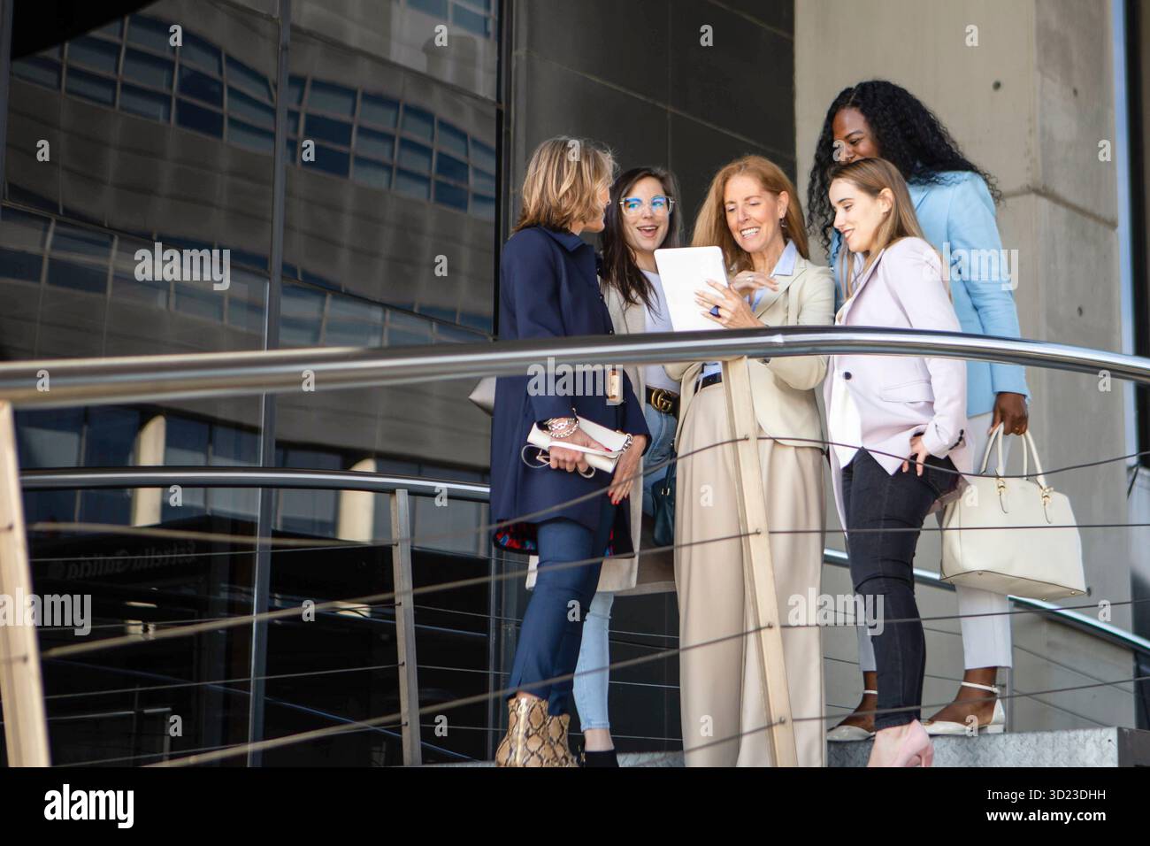 Eine Gruppe von fünf Frauen nahm an einem sonnigen Nachmittag an einem Gespräch auf dem Balkon eines modernen Gebäudes teil. Sie sind stilvoll gekleidet und scheinen s zu sein Stockfoto